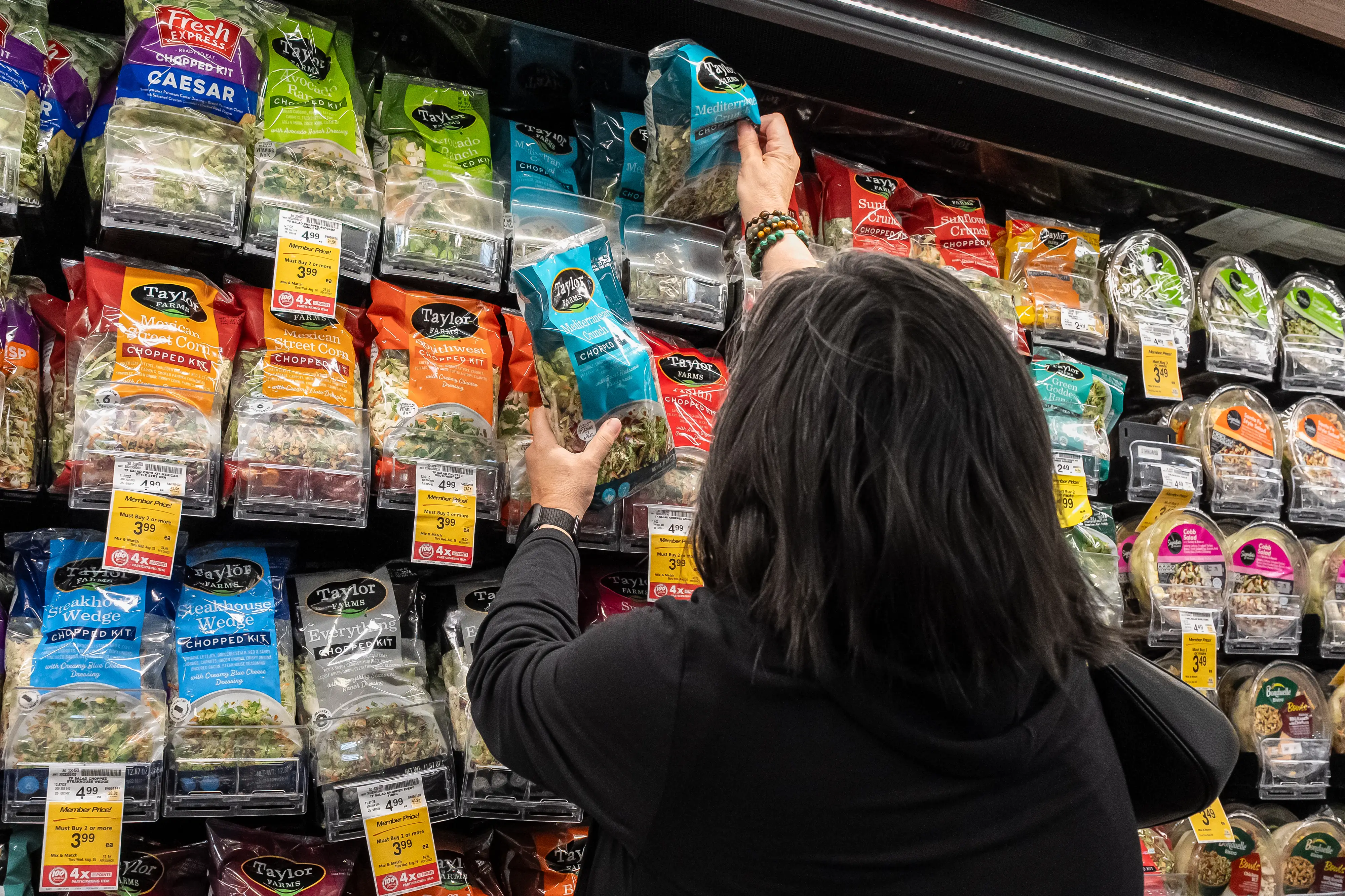 A customer reaches for Taylor Farms bagged salads for sale at a grocery store