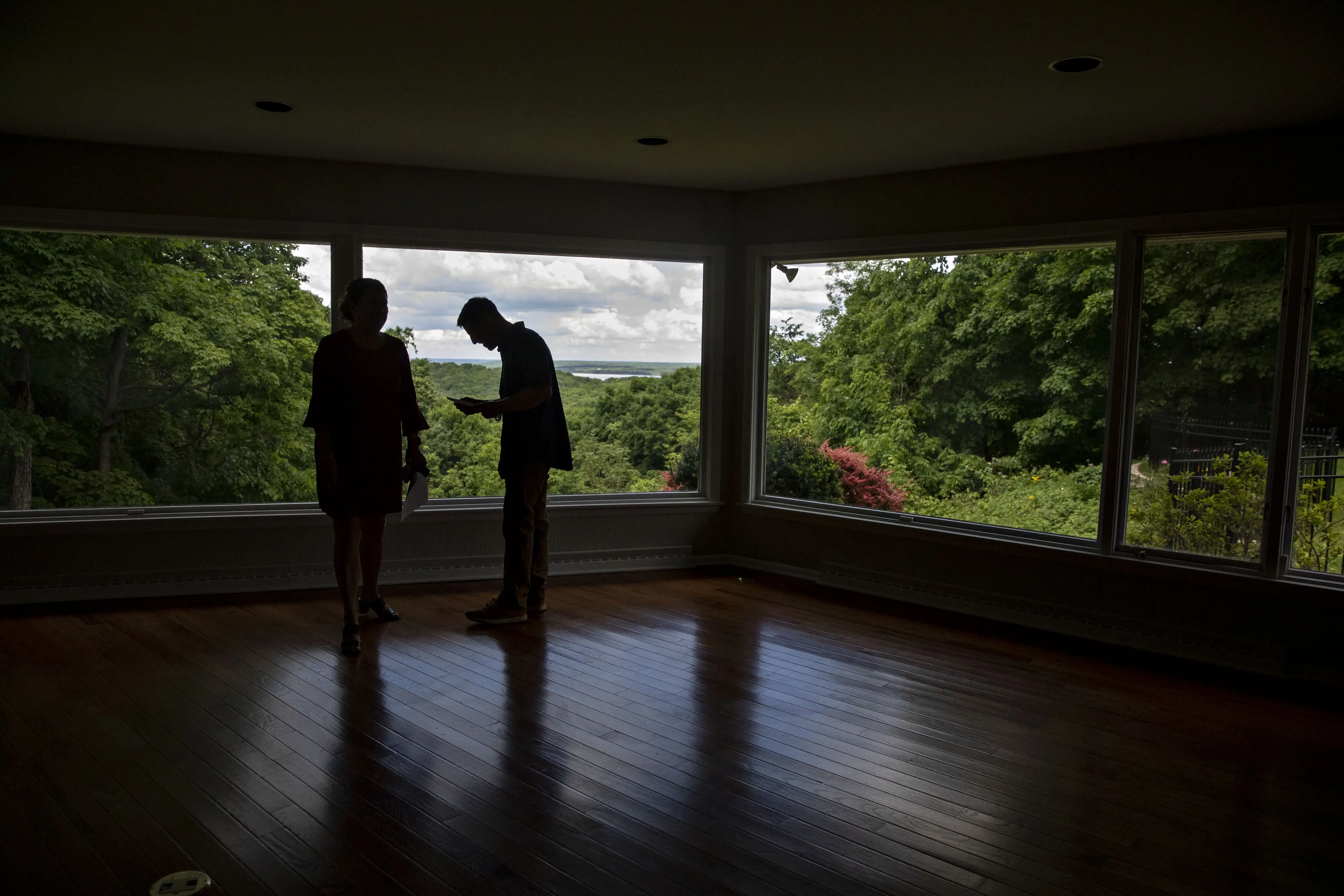 Silhouettes of two potential buyers against the window of an empty house during a tour.