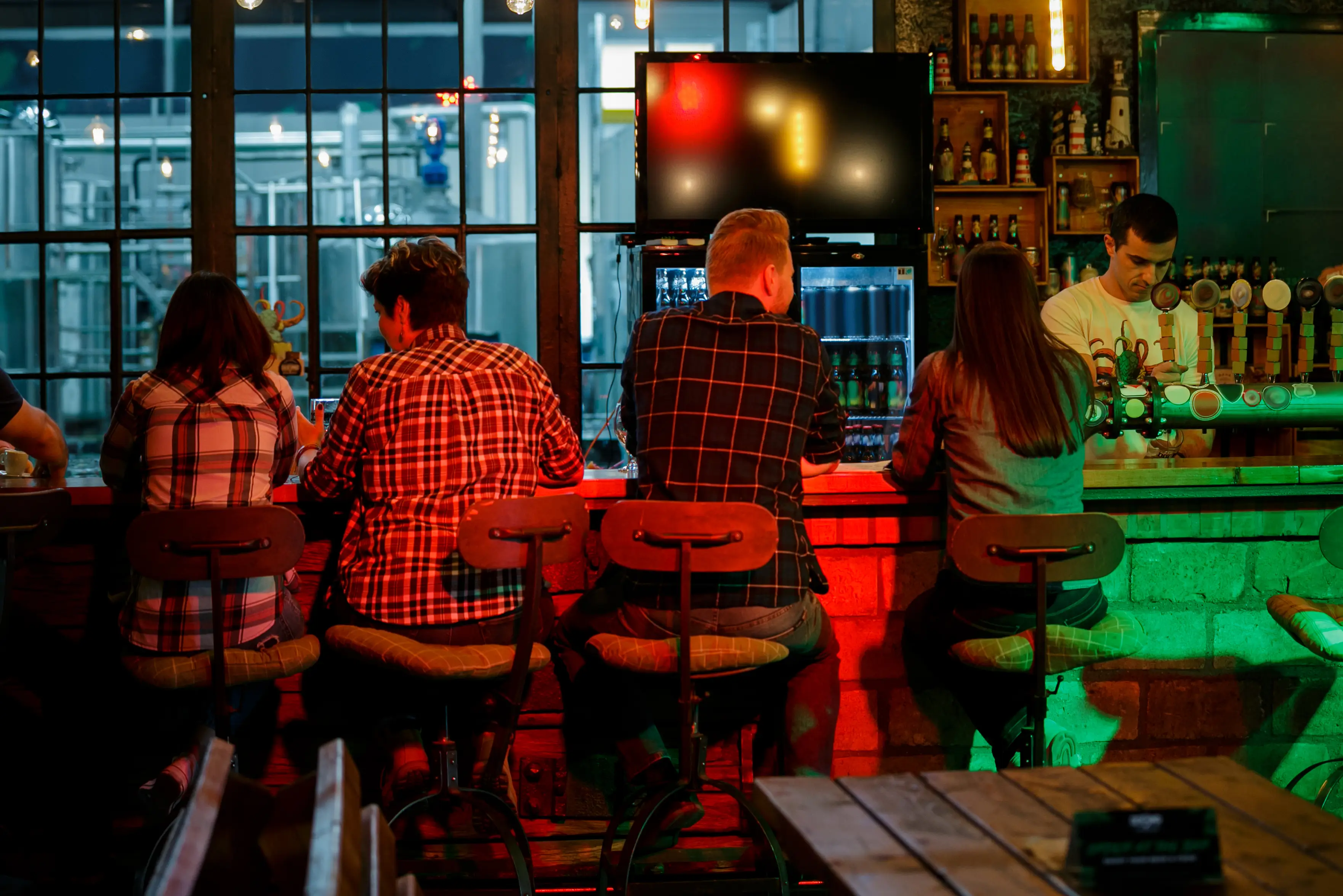 Rear view of people sitting at the bar counter in a pub, bartender pouring drinks