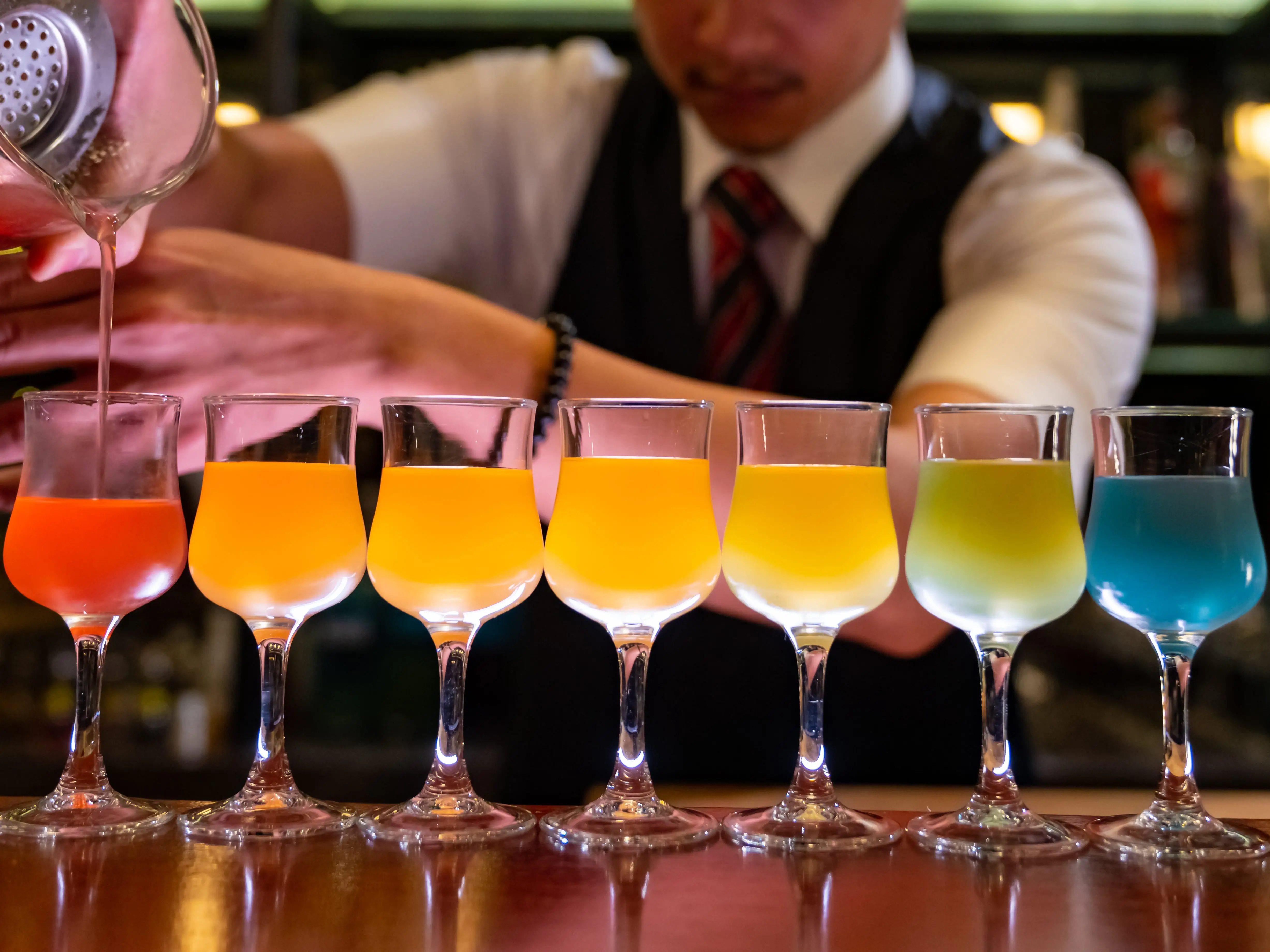 Bartender pouring colorful row of drinks