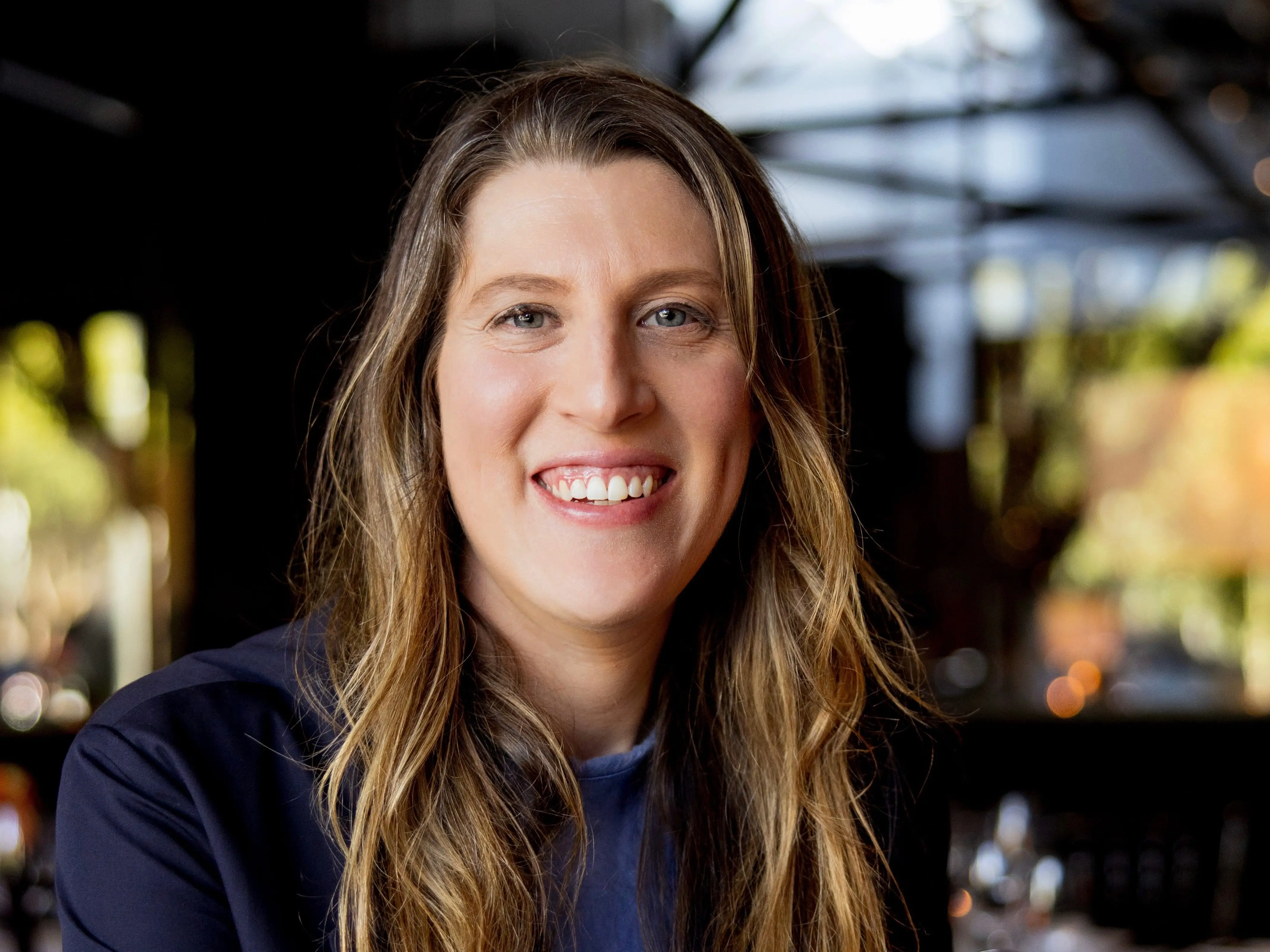 Mother Ventures' Allison Stern sits at a table smiling with a blue jacket and shirt.