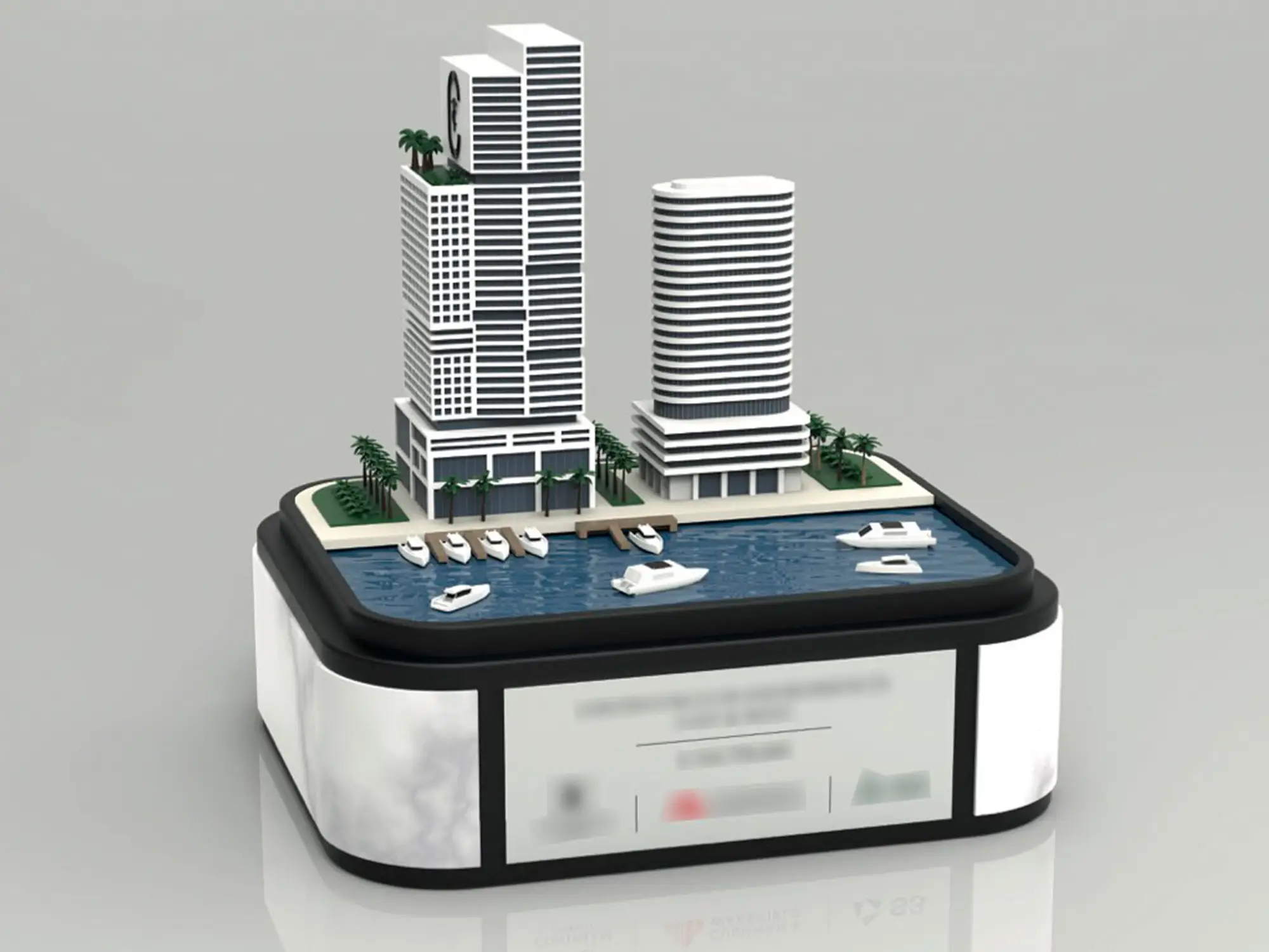 Miniature waterfront development model with high-rise towers, palm trees and boats displayed on a tablet-like base.
