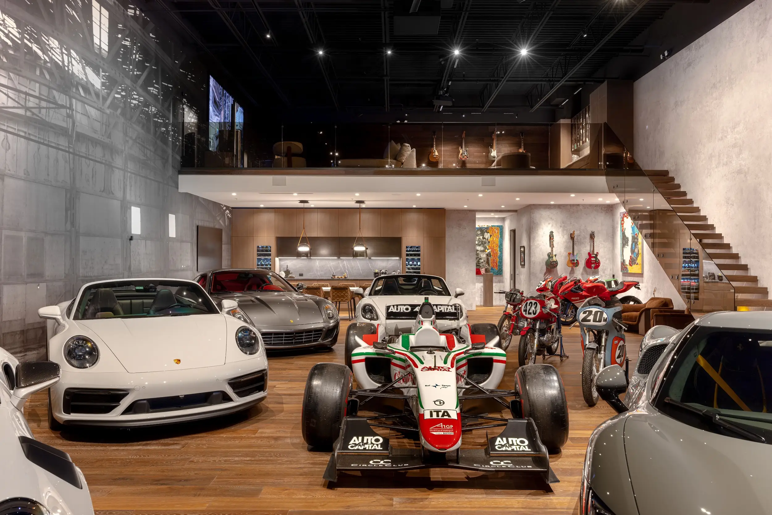 Luxury garage showroom displays sports cars, an open-wheel race car, motorcycles, and a mezzanine lounge.