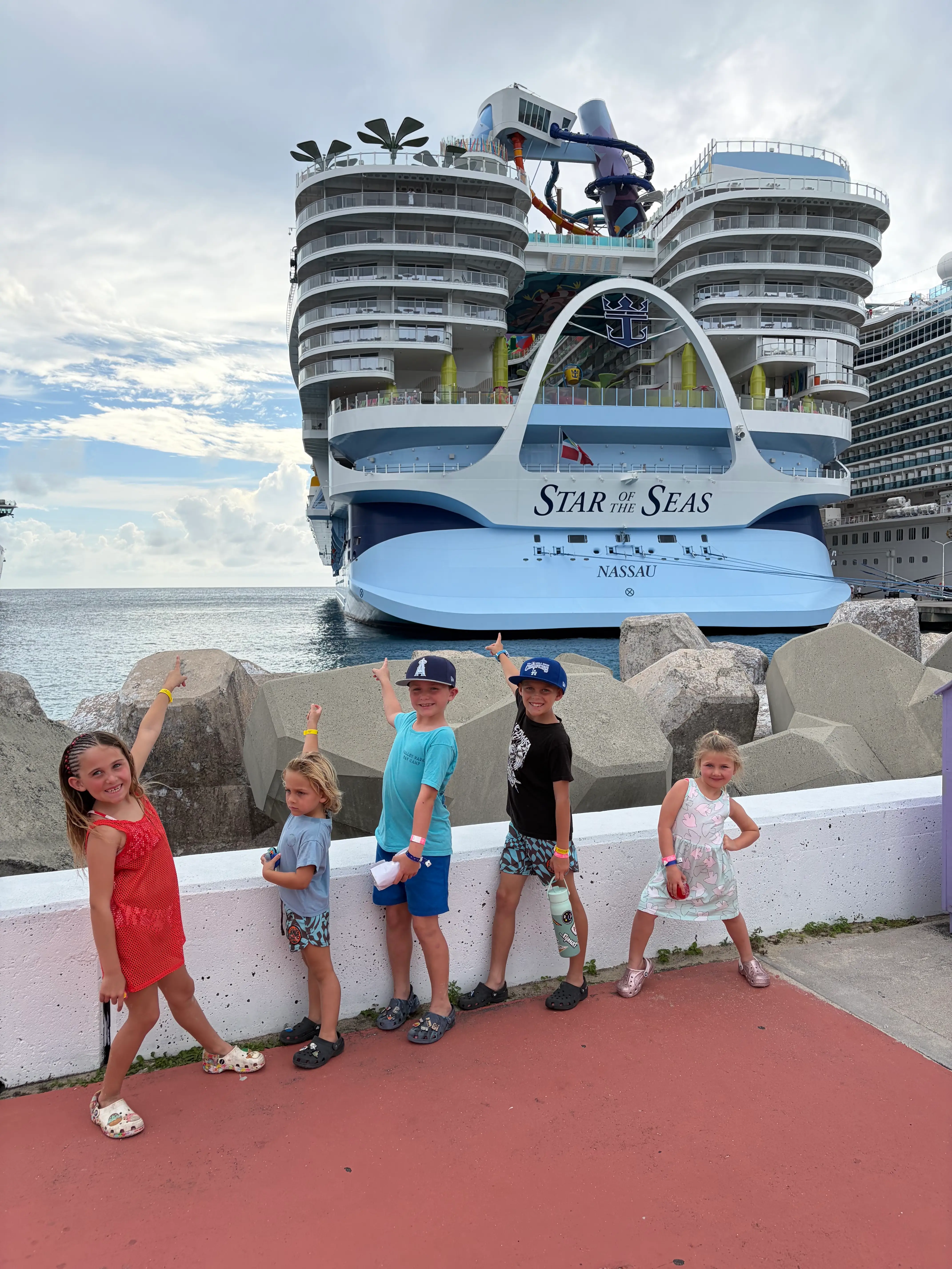 Five kids stand on a dock next to the Star of the Seas cruise ship.