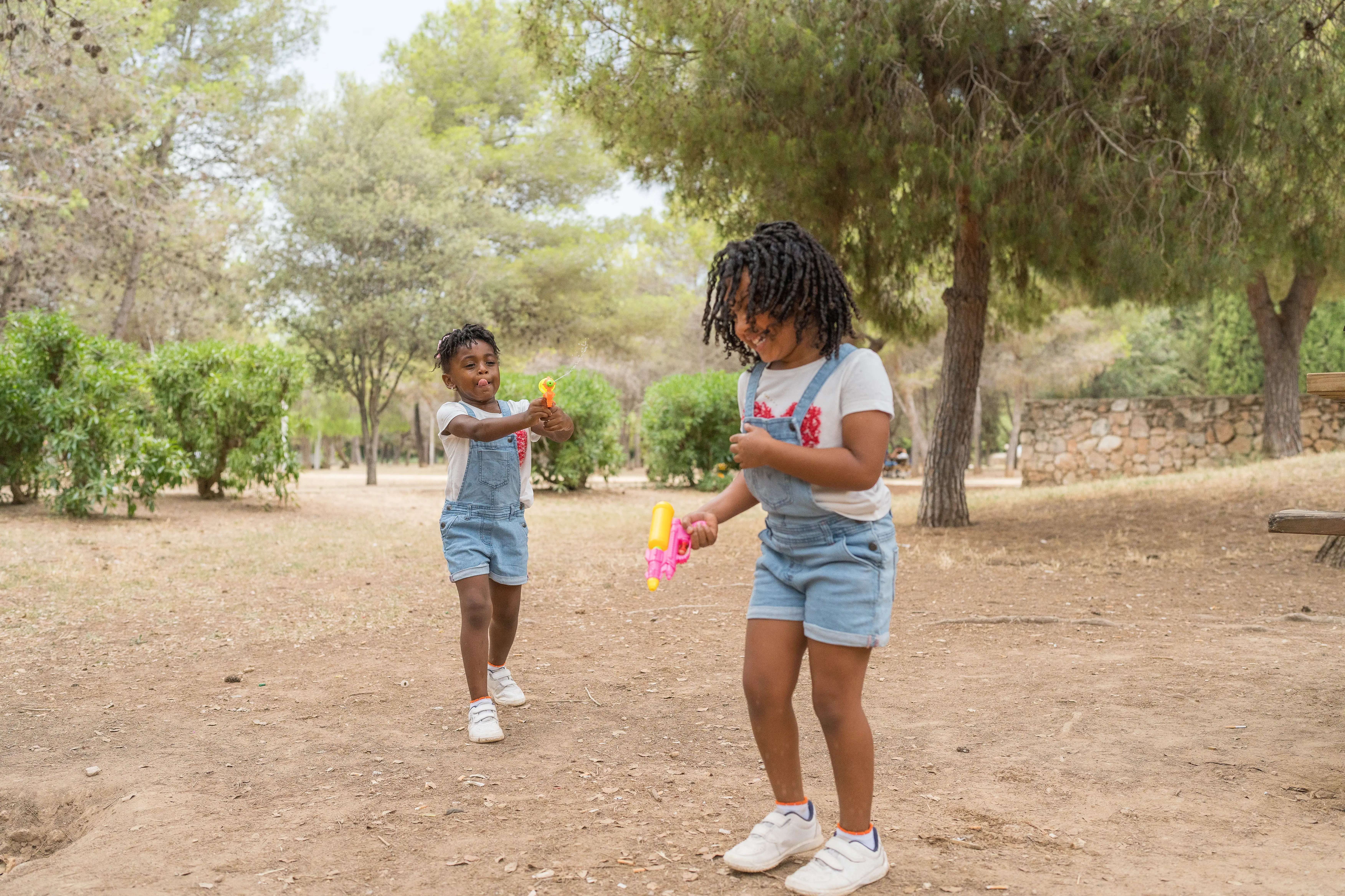 two kids in overalls playing outside by trees