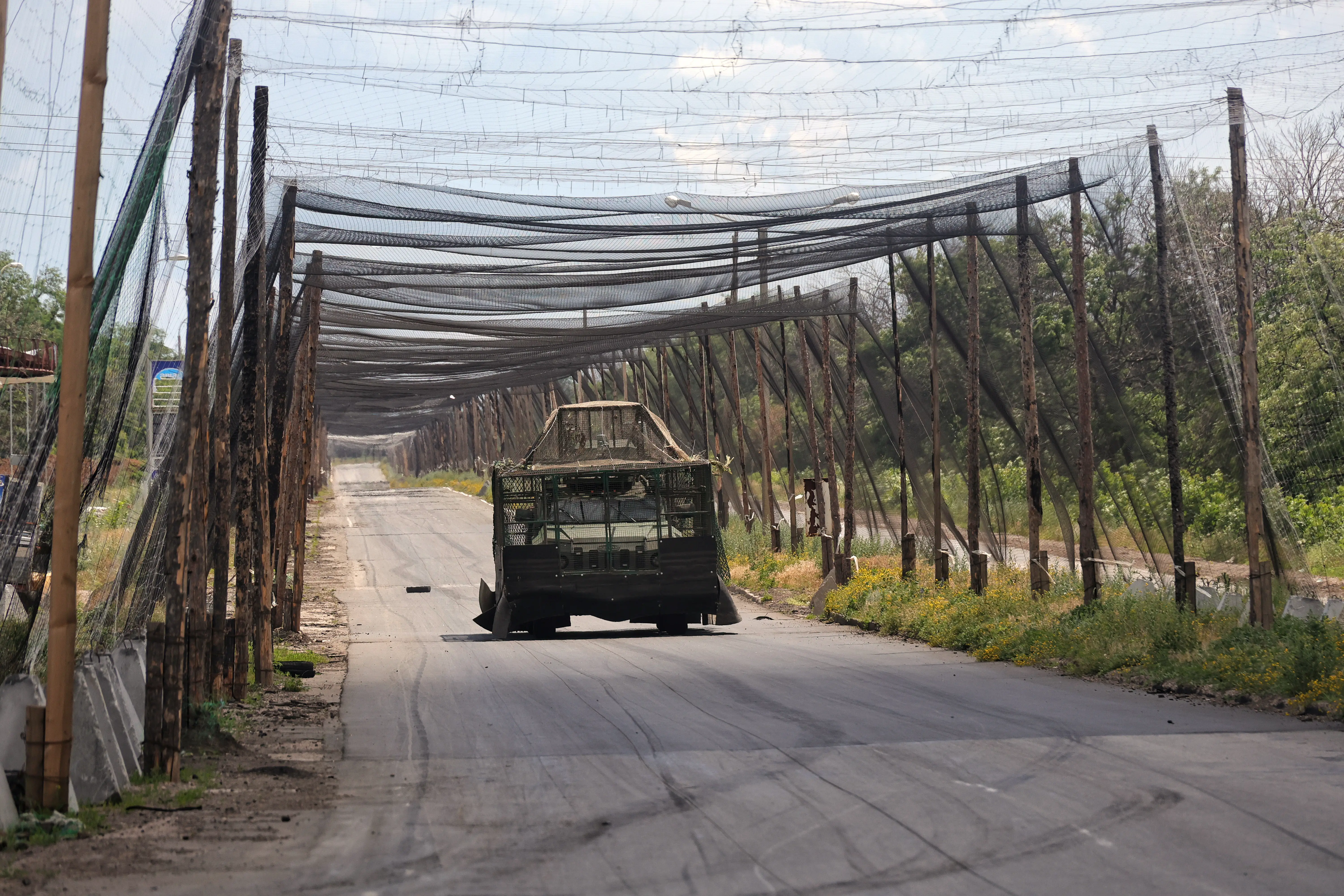 An armored military vehicle equipped with additional protection against drone strikes travels along a road shielded by anti-drone nets in the Donetsk region, Ukraine, on June 20, 2026.