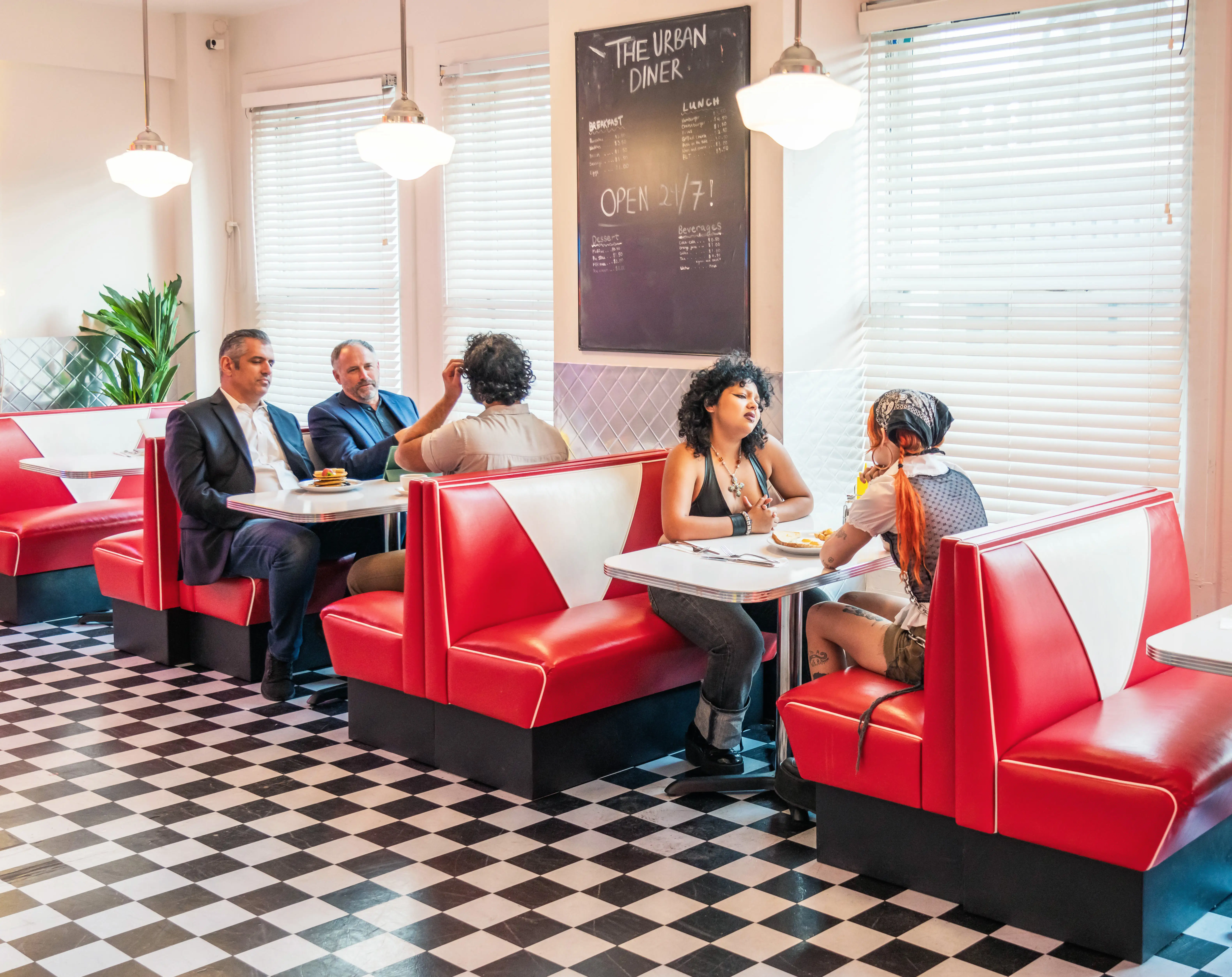 Patrons sit in red booths inside a bright retro diner with checkered flooring and a chalkboard menu.