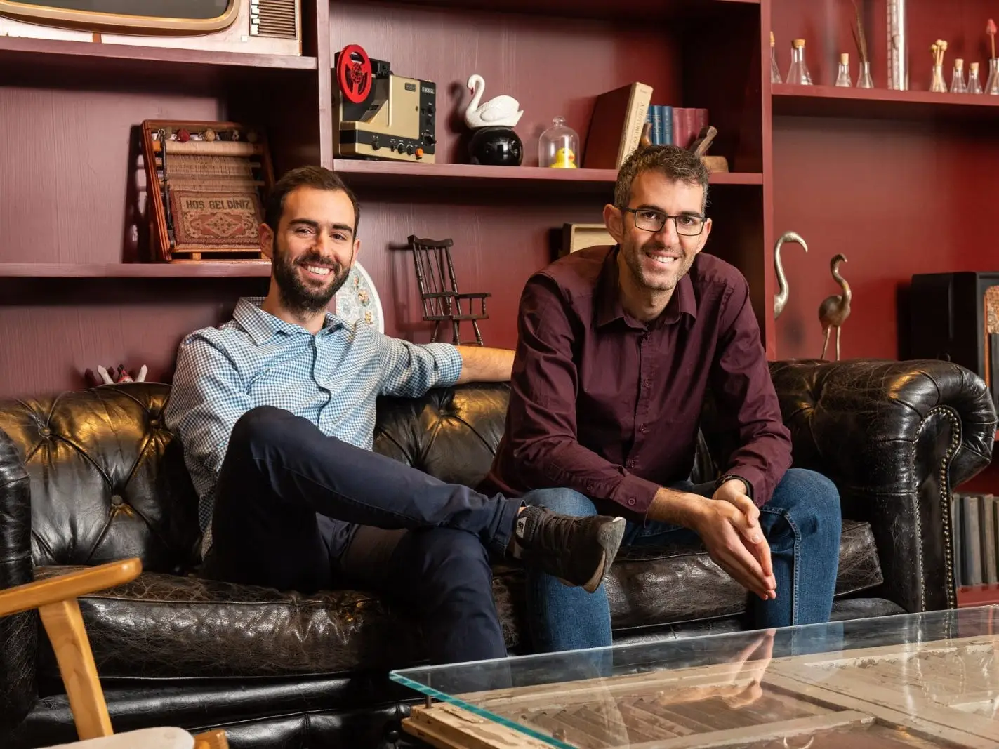 Harmony cofounders Ran Ribenzaft and Nitzan Shapira, sitting on a leather couch in front of maroon shelves.