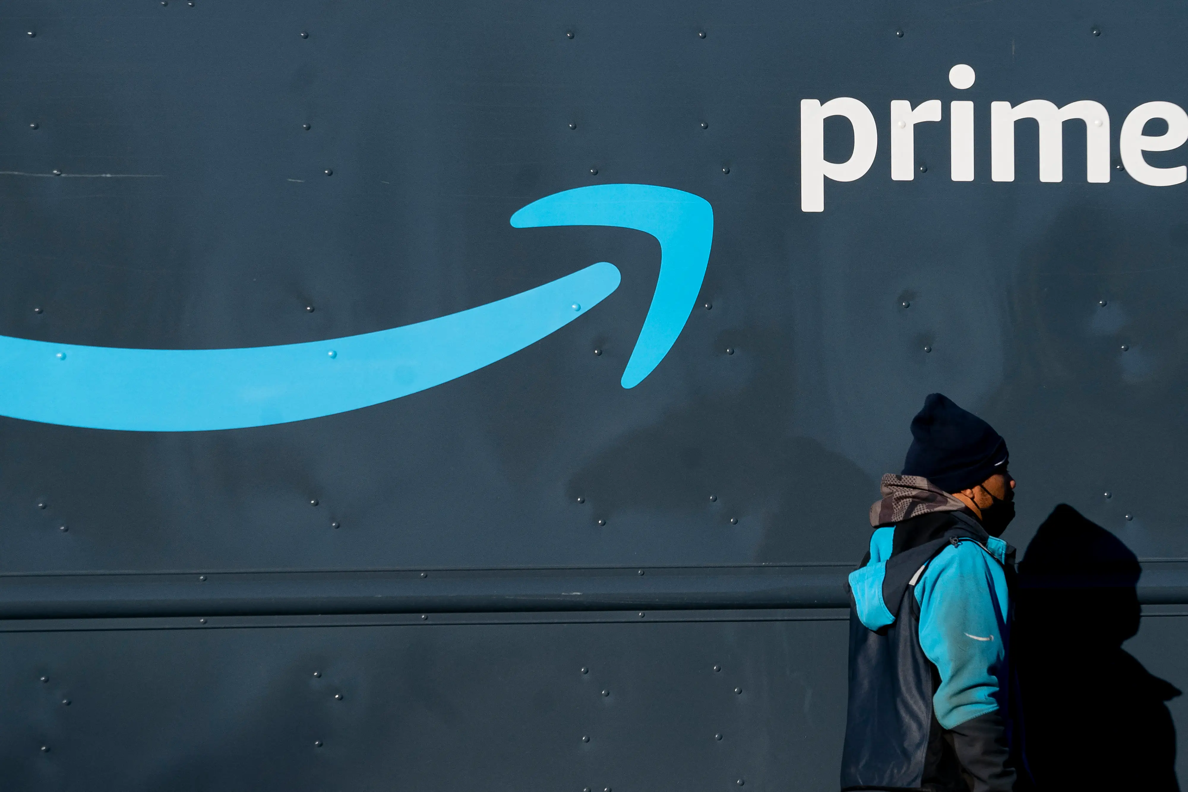 A person walks past a dark Amazon Prime vehicle with the blue smile logo and white “prime” text.