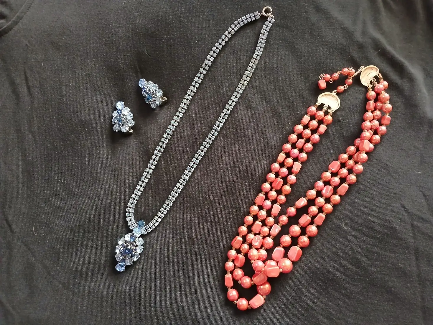 Earrings and a matching necklace shown next to a few strands of peach beads.