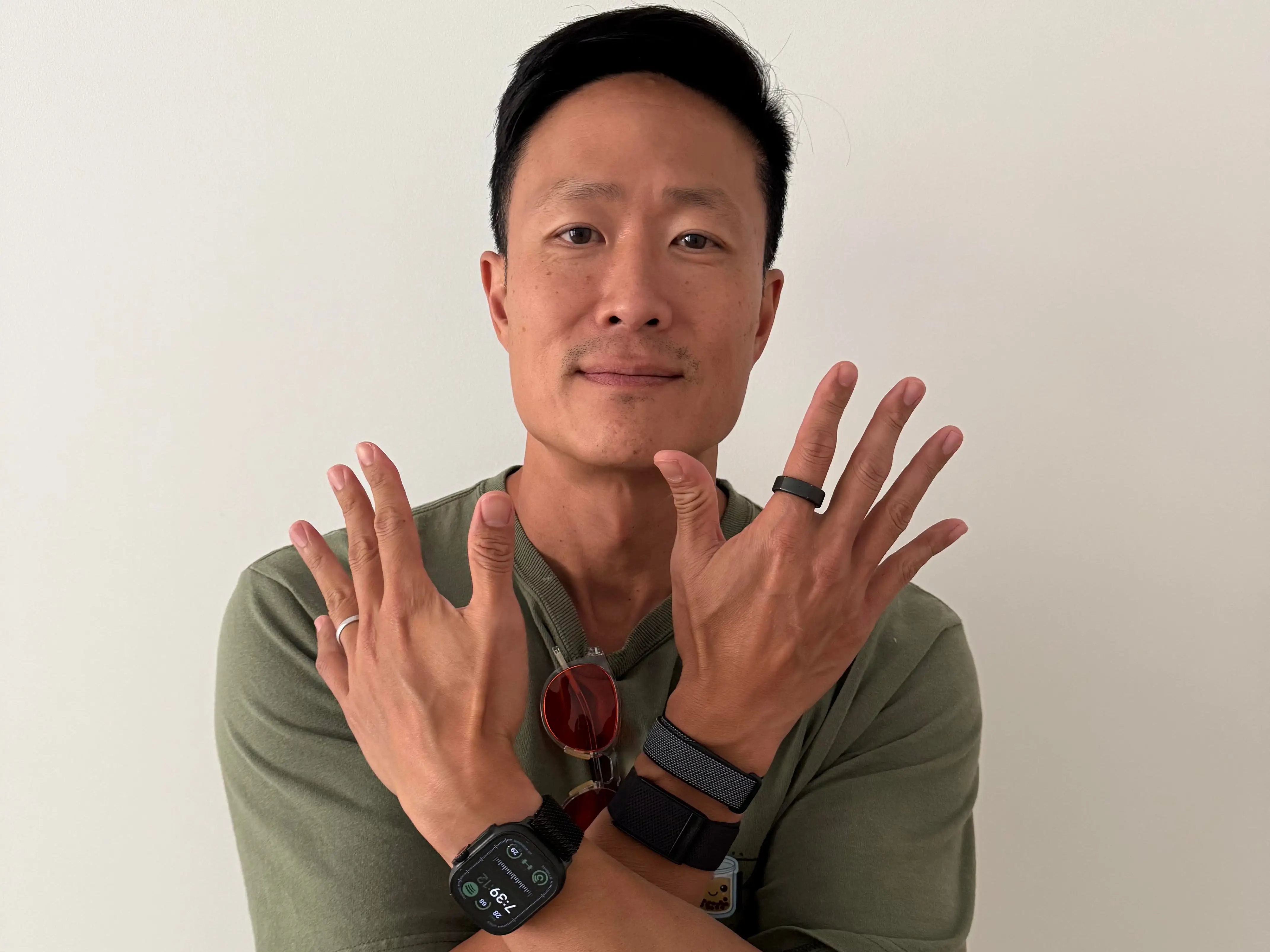 Person in a green shirt crosses arms to display 4 different fitness trackers he's wearing at once