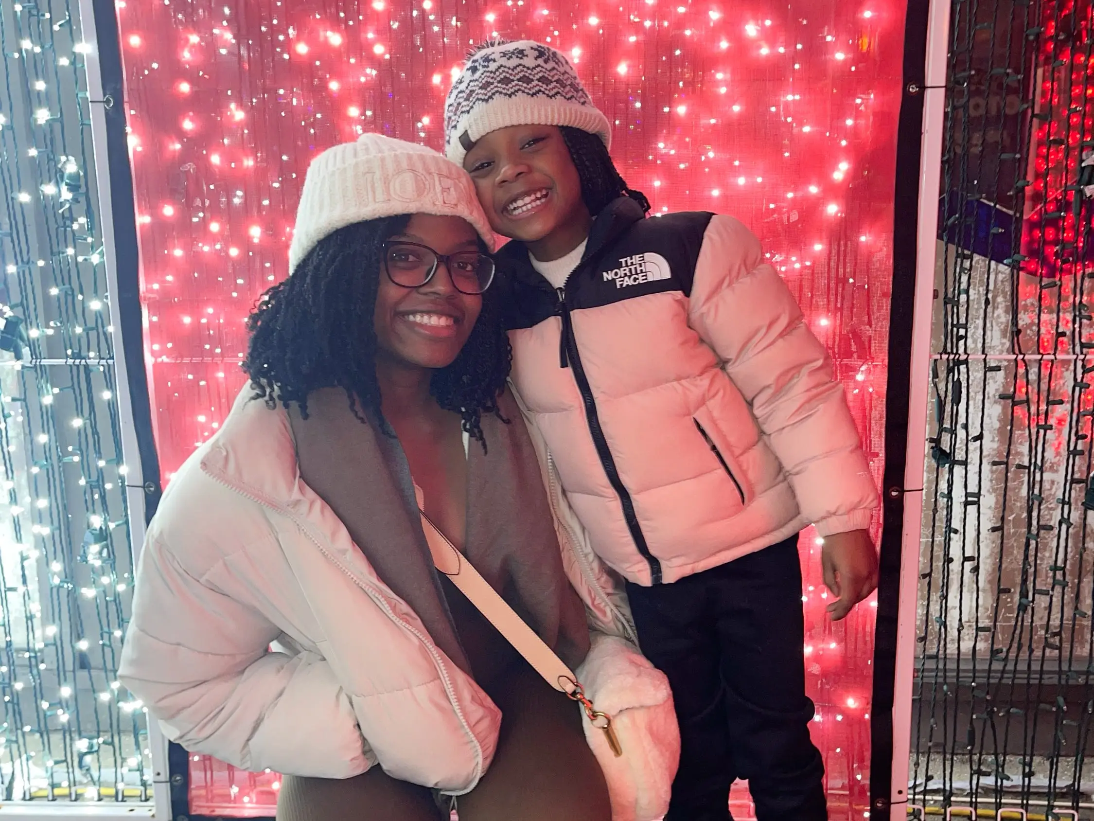 The writer and her niece, in winter clothing, pose in front of red-and-white holiday lights.
