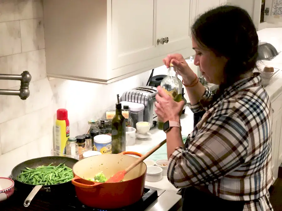 Person cooks at a kitchen stove with green beans in a skillet and a red Dutch oven nearby.