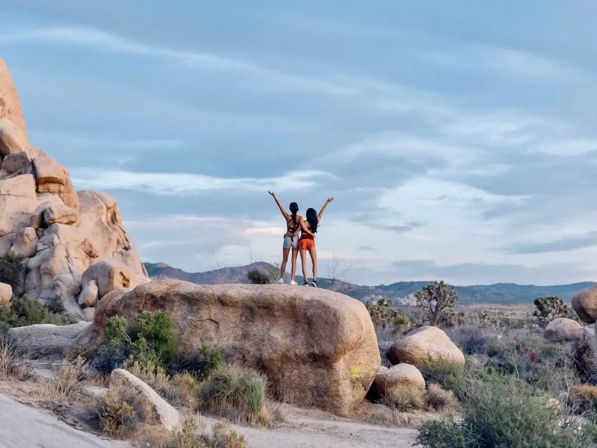 Sharon and a friend stand on a rock in the desert with their arms stretched up.