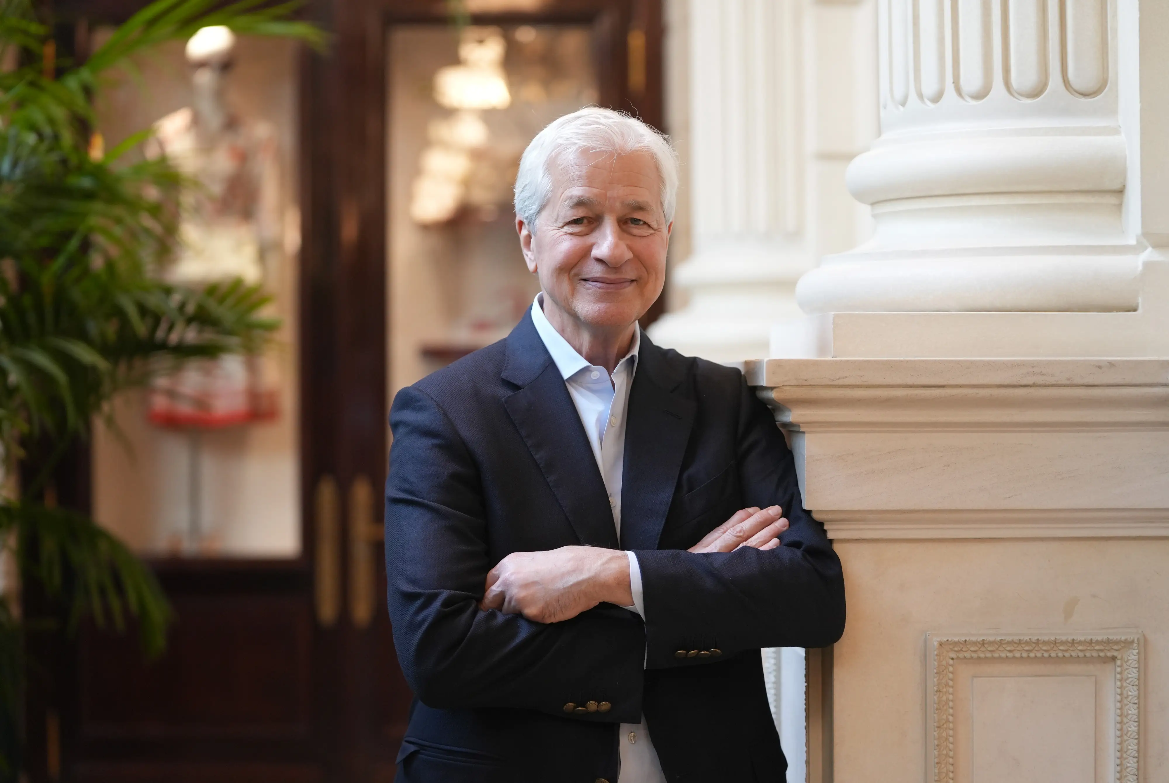 Jamie Dimon, CEO of JPMorgan, wearing a suit, arms folded, smiling.