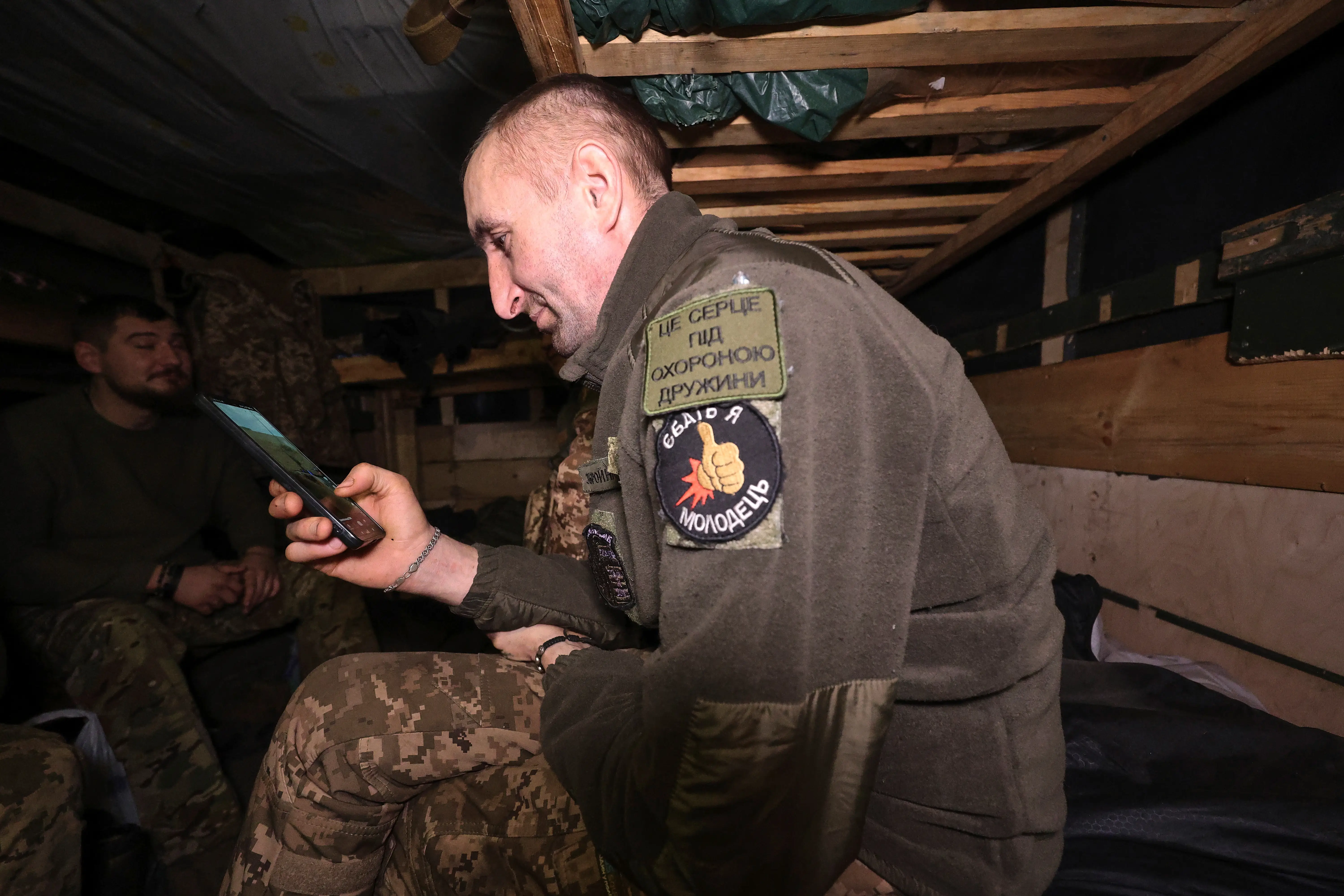 A Ukrainian soldier scrolls through videos on his phone inside a bunker.