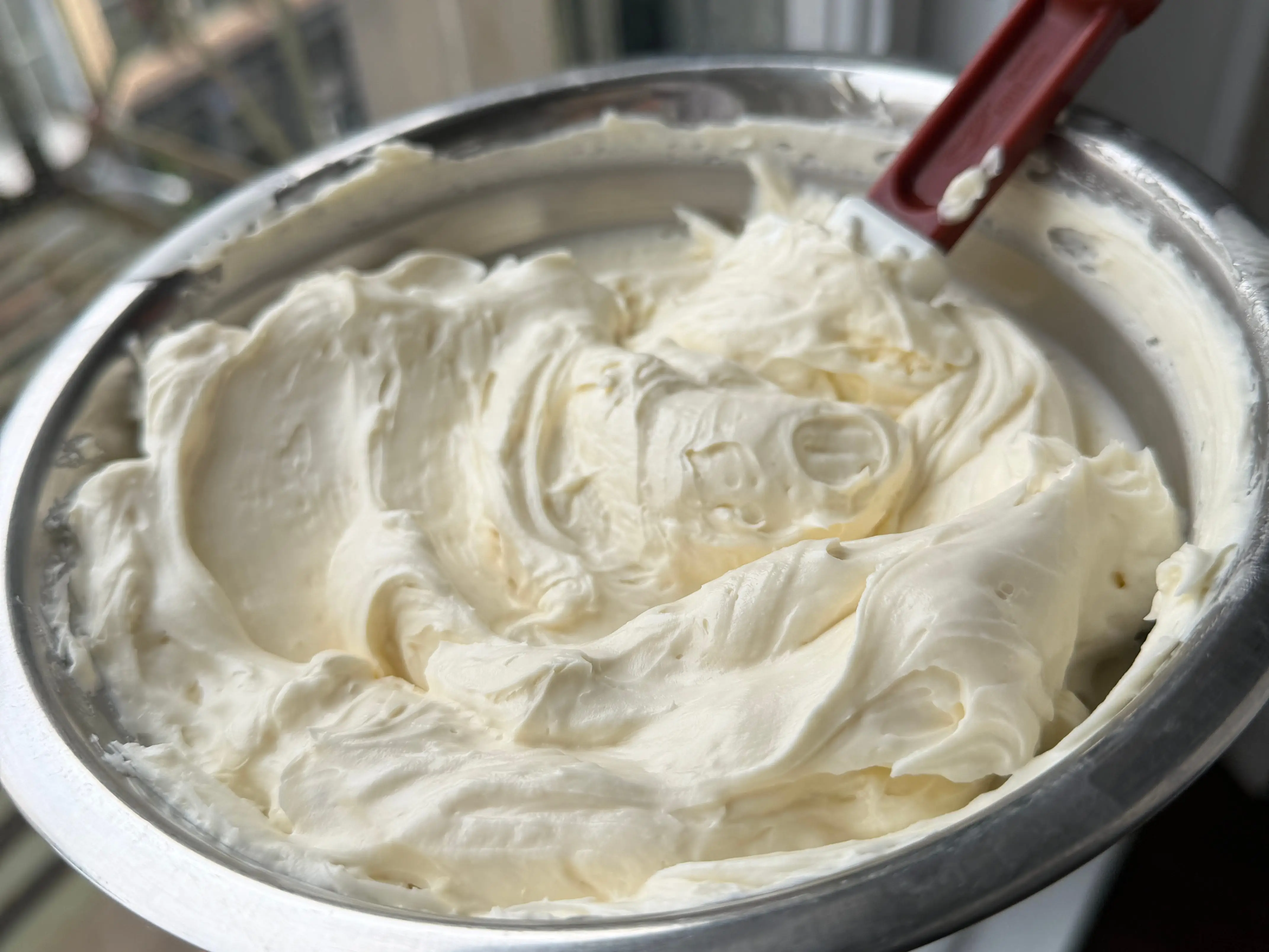 The writer holding a mixing bowl filled with thick white frosting and a red spatula.