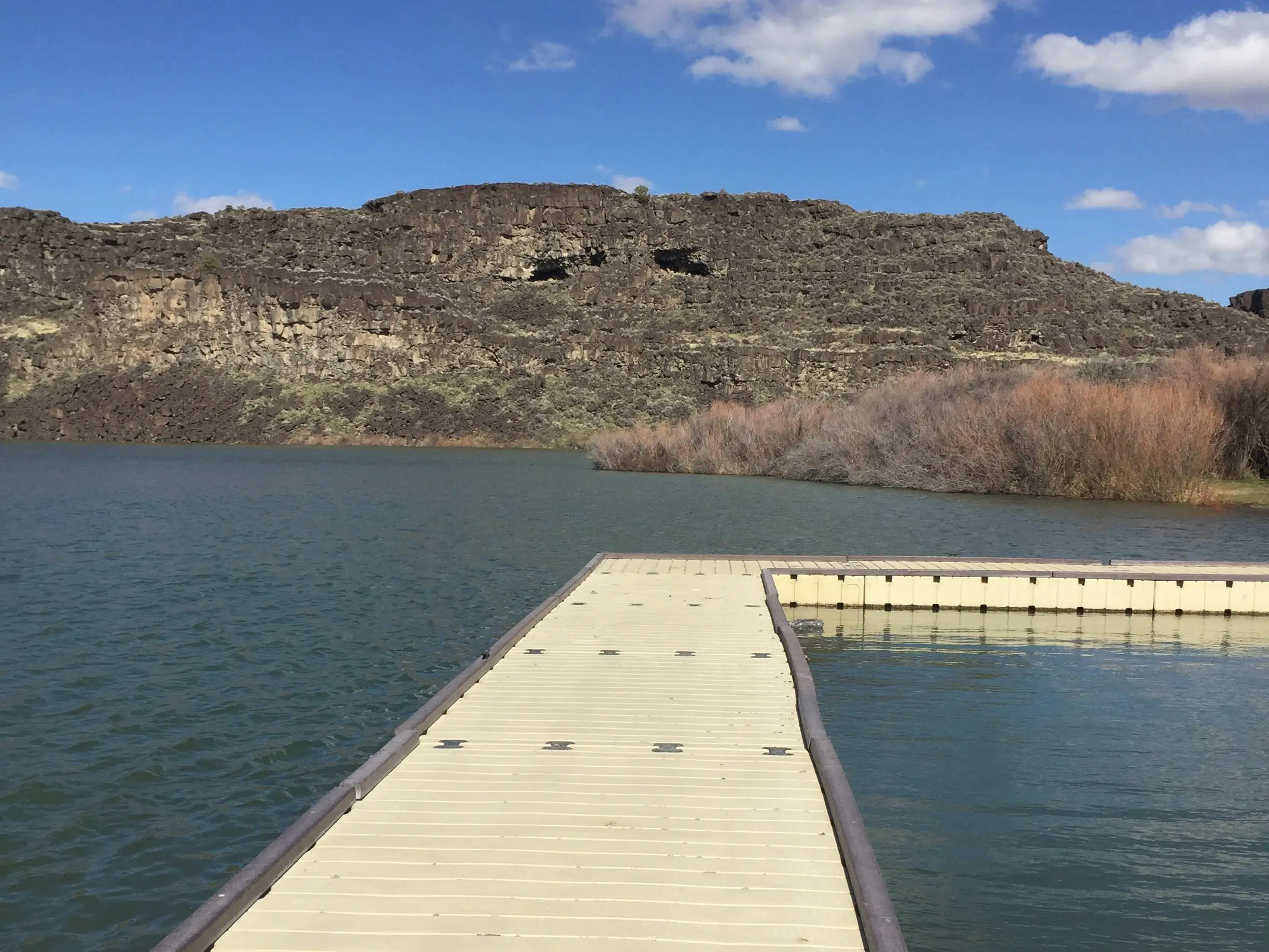A floating dock extends into a lake beneath rocky cliffs.