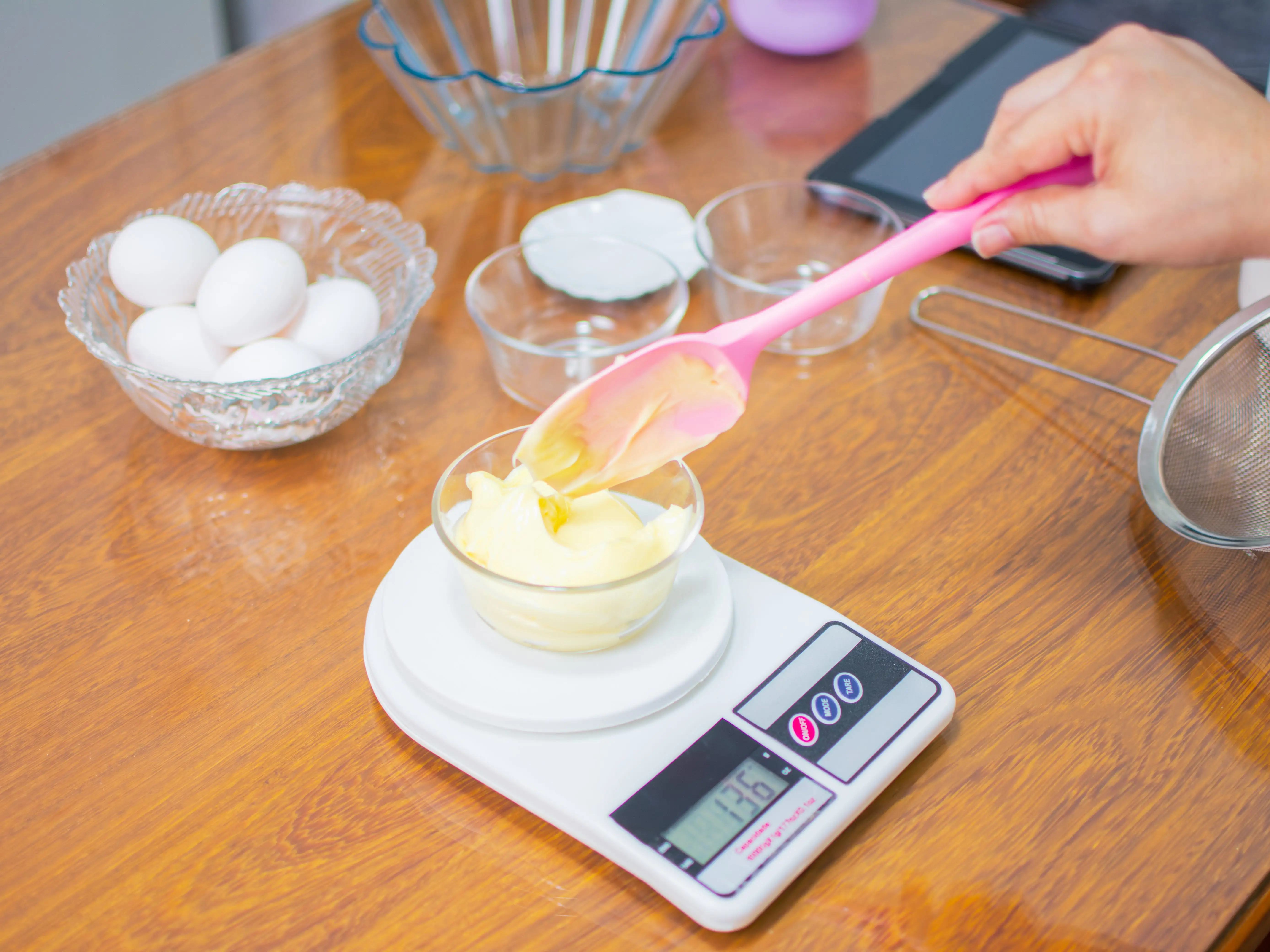 A person using a pink spatula to measure a baking ingredient on a digital kitchen scale.