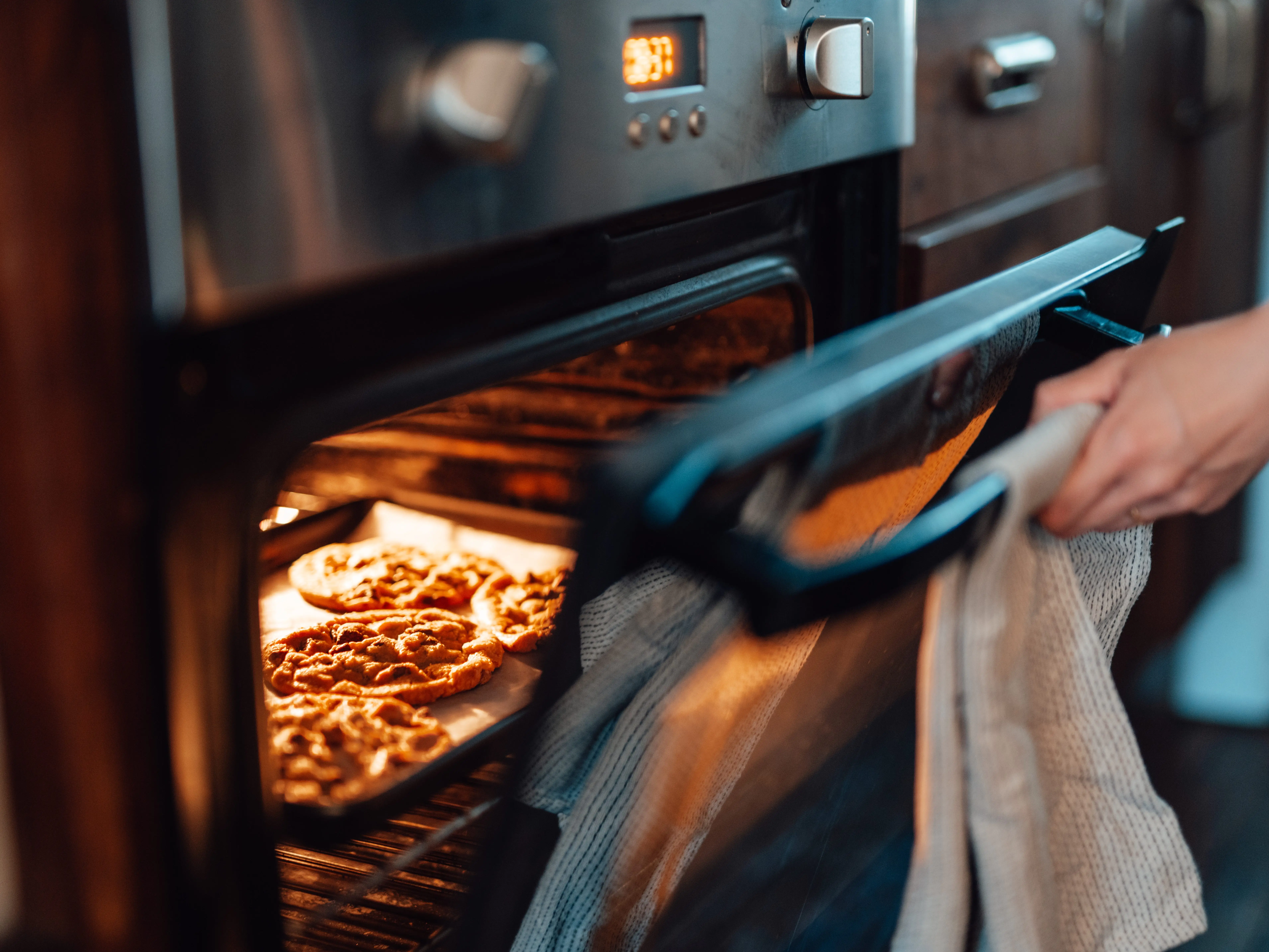 A person opening up an oven while a sheet of cookies are baking.