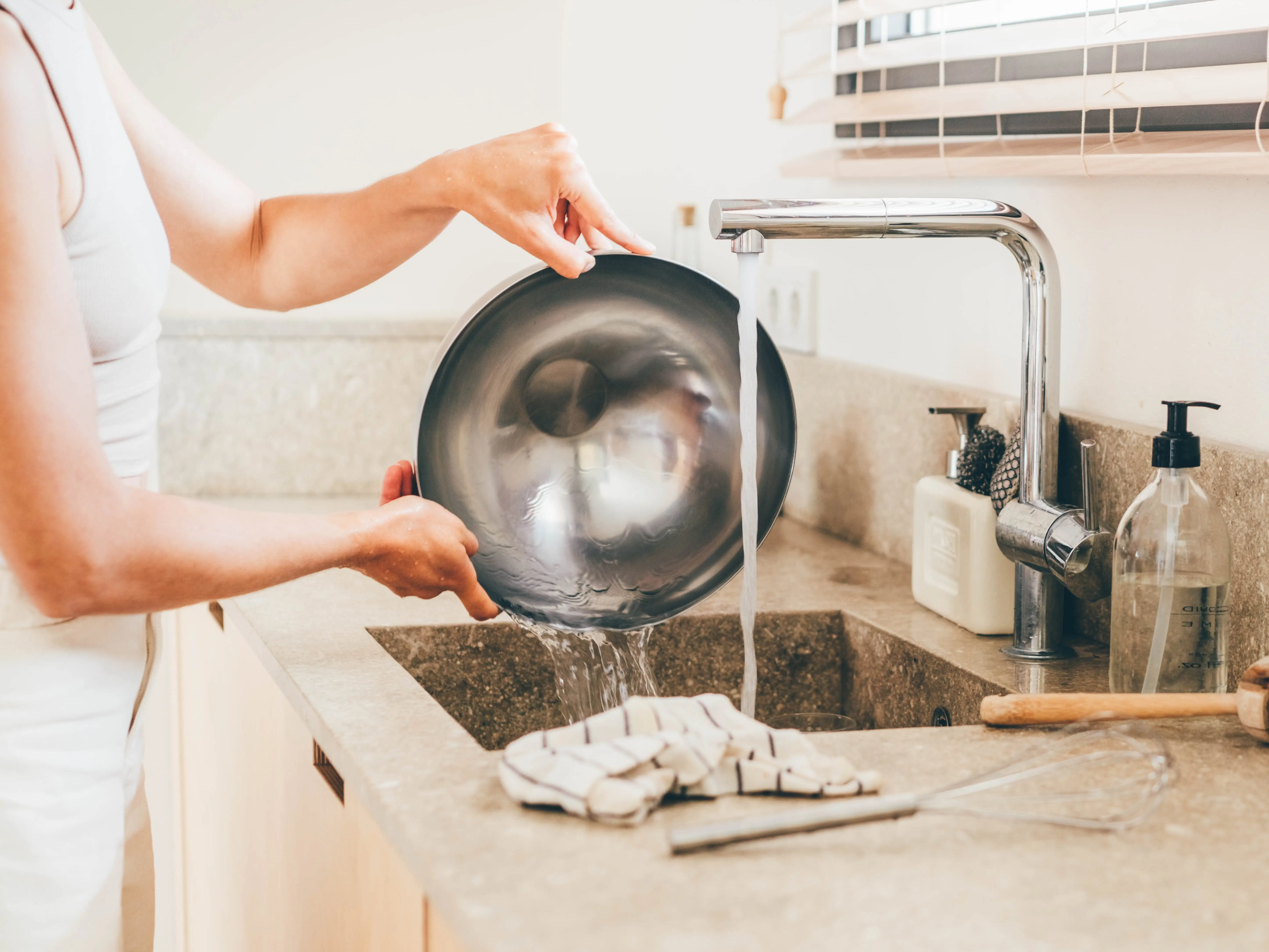 A woman rinsing a metal baking bowl in the sink.