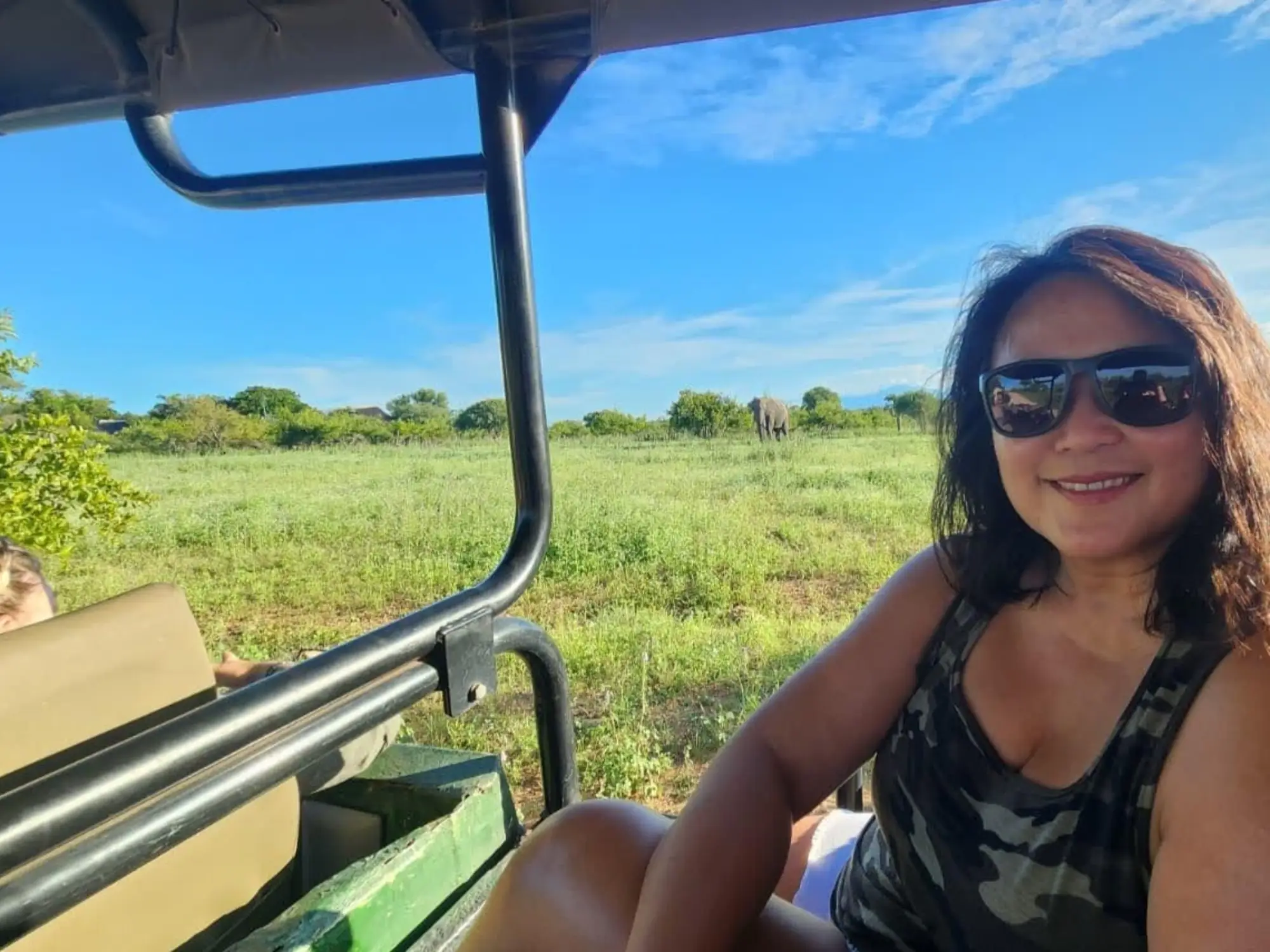 Woman in open-air vehicle in Africa smiling with elephant in background