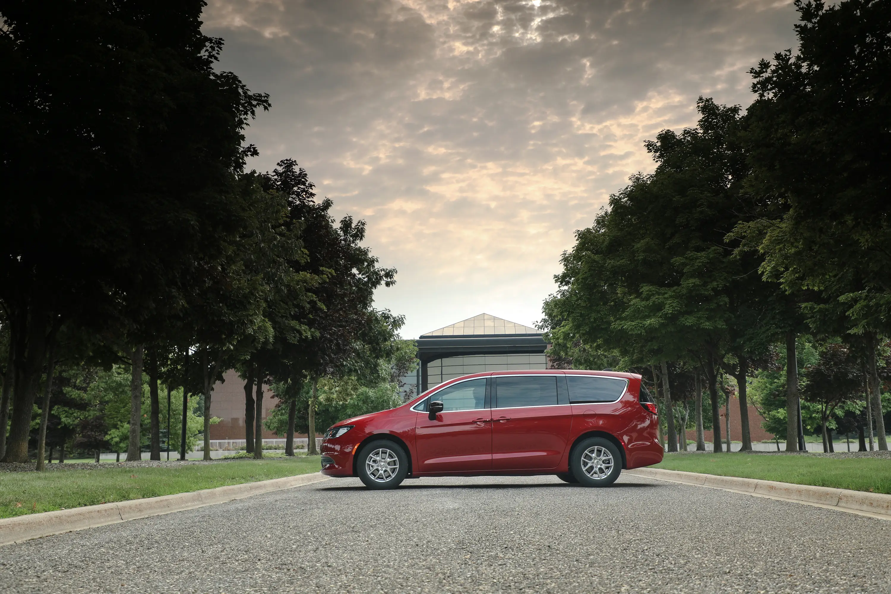 A red Chrysler Voyager is parked on a tree-lined street.