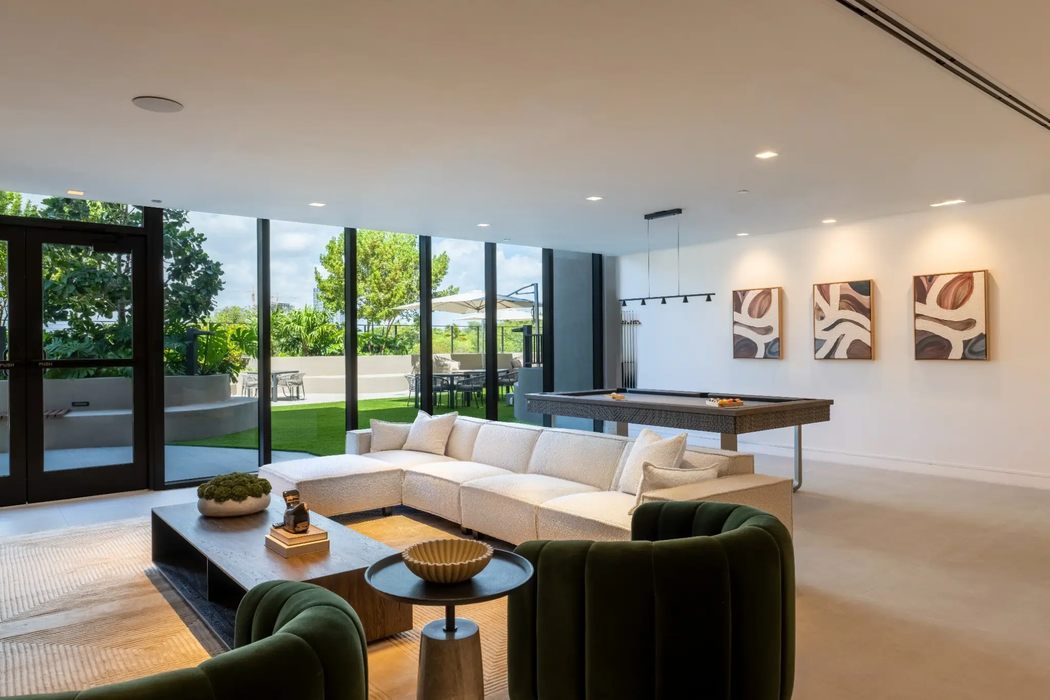 Modern lounge with sectional sofa, green chairs, pool table, wall art, and glass doors opening to a patio.