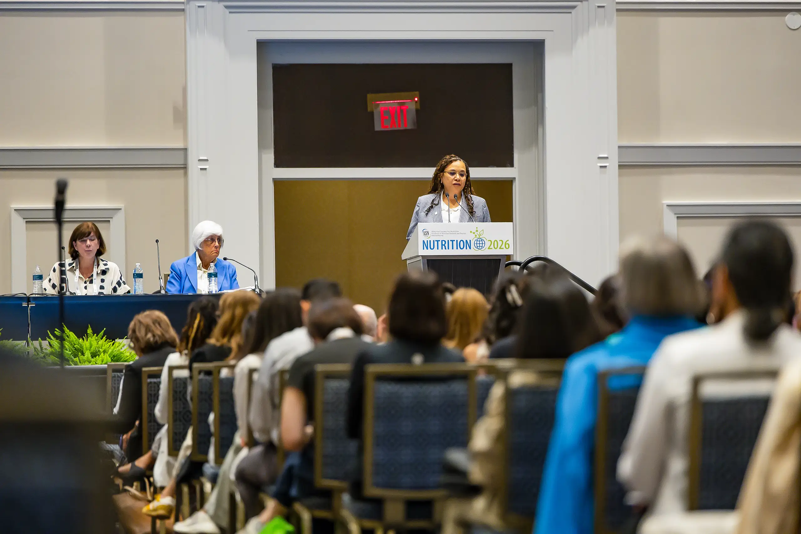 Speaker addresses an audience from a NUTRITION 2026 podium during a conference session in a ballroom.