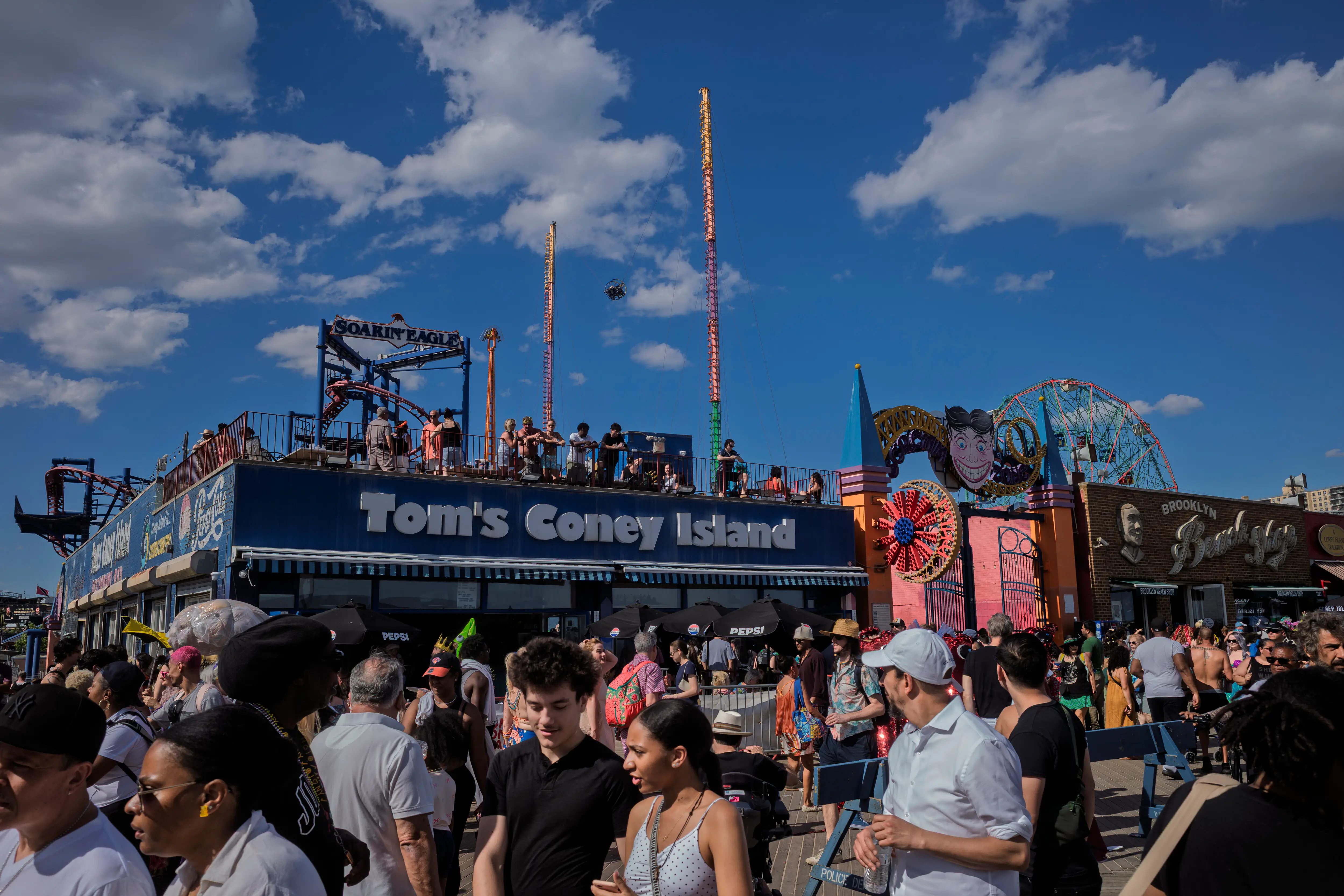 People on the Coney Island boardwalk, next to Tom's Coney Island and the Brooklyn Beach Shop.