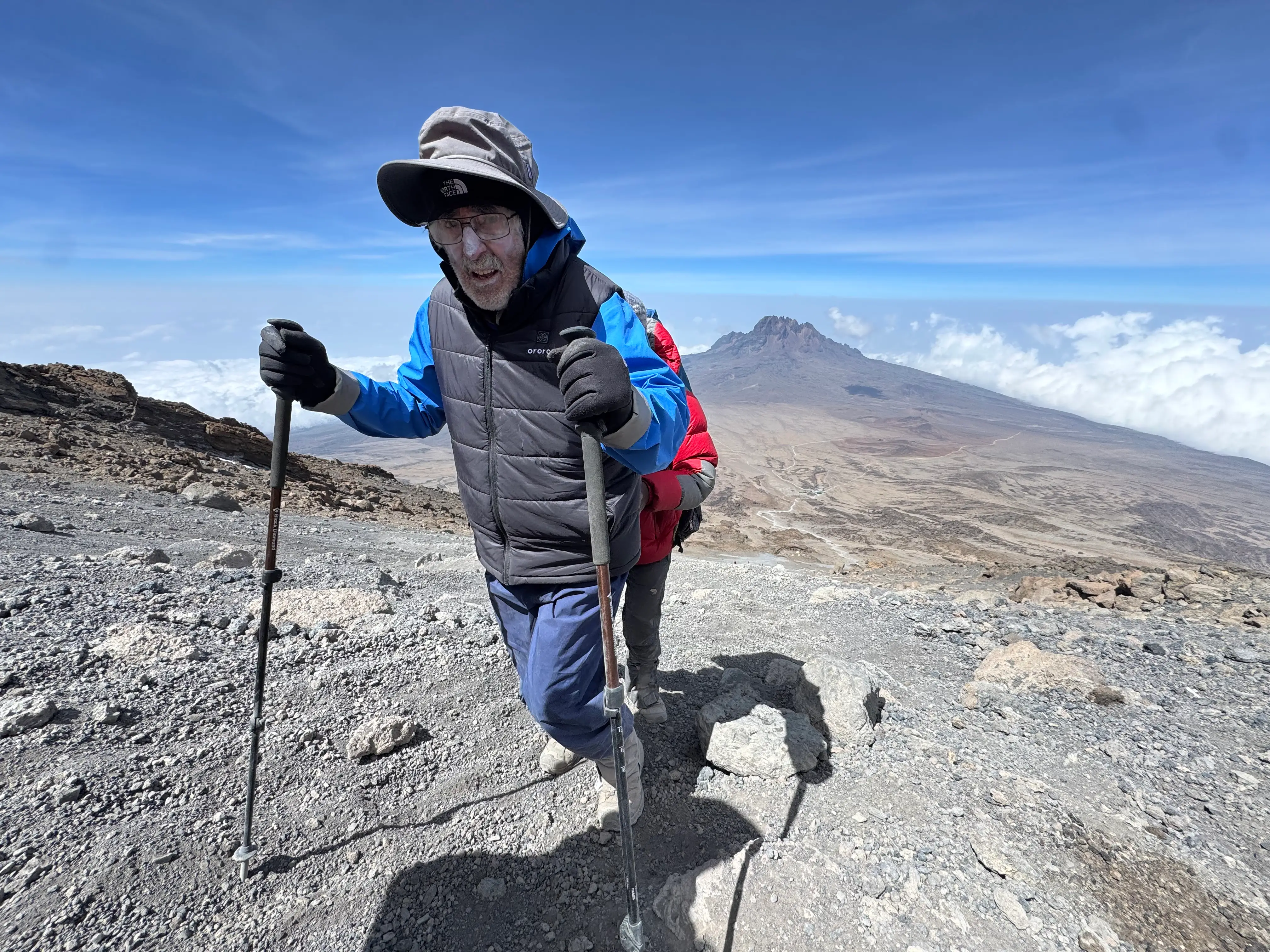 A senior climbing Kilimanjaro using hiking sticks.