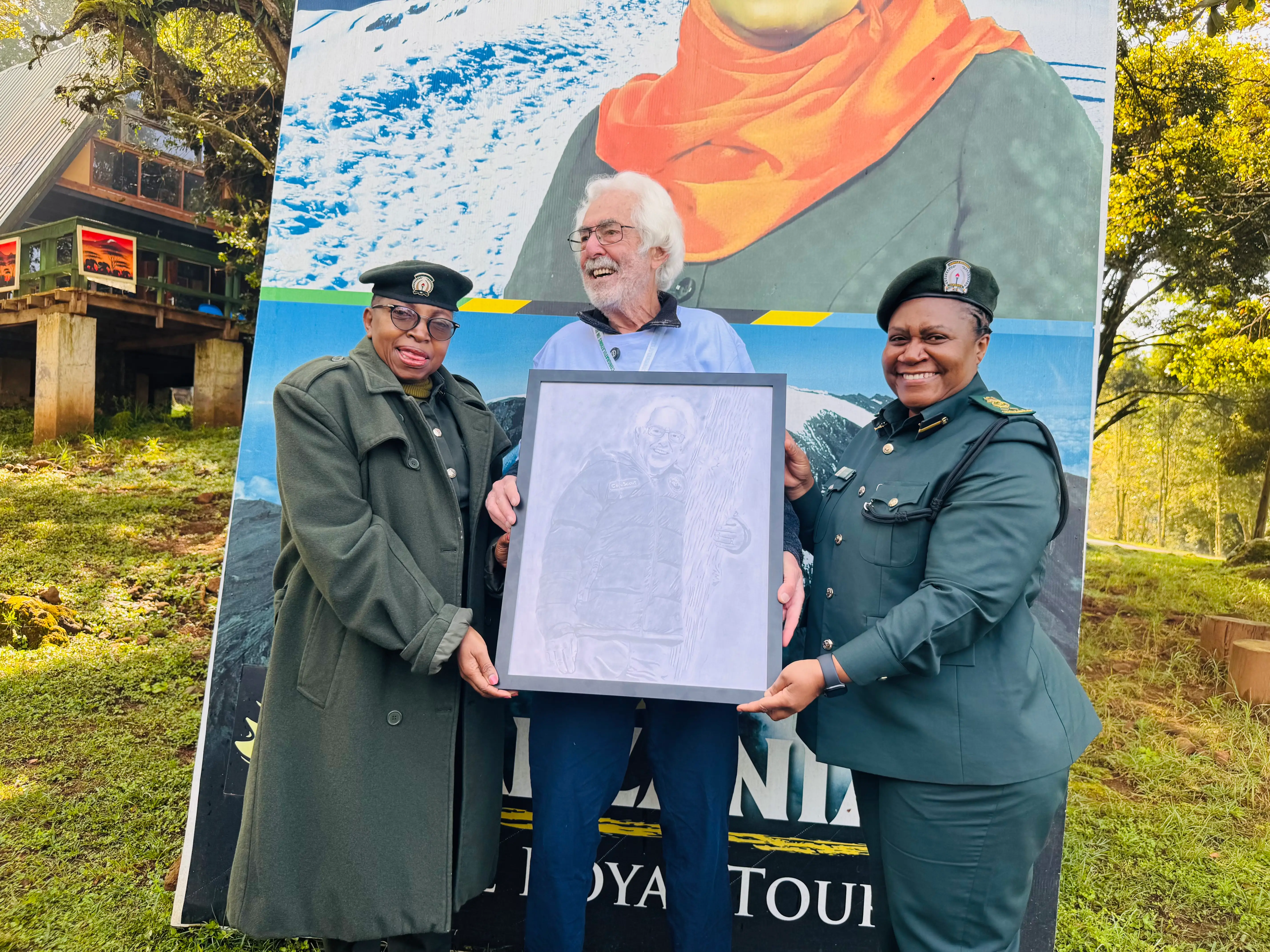 An older man is being presented with a portrait of himself at the foot of Kilimanjaro.