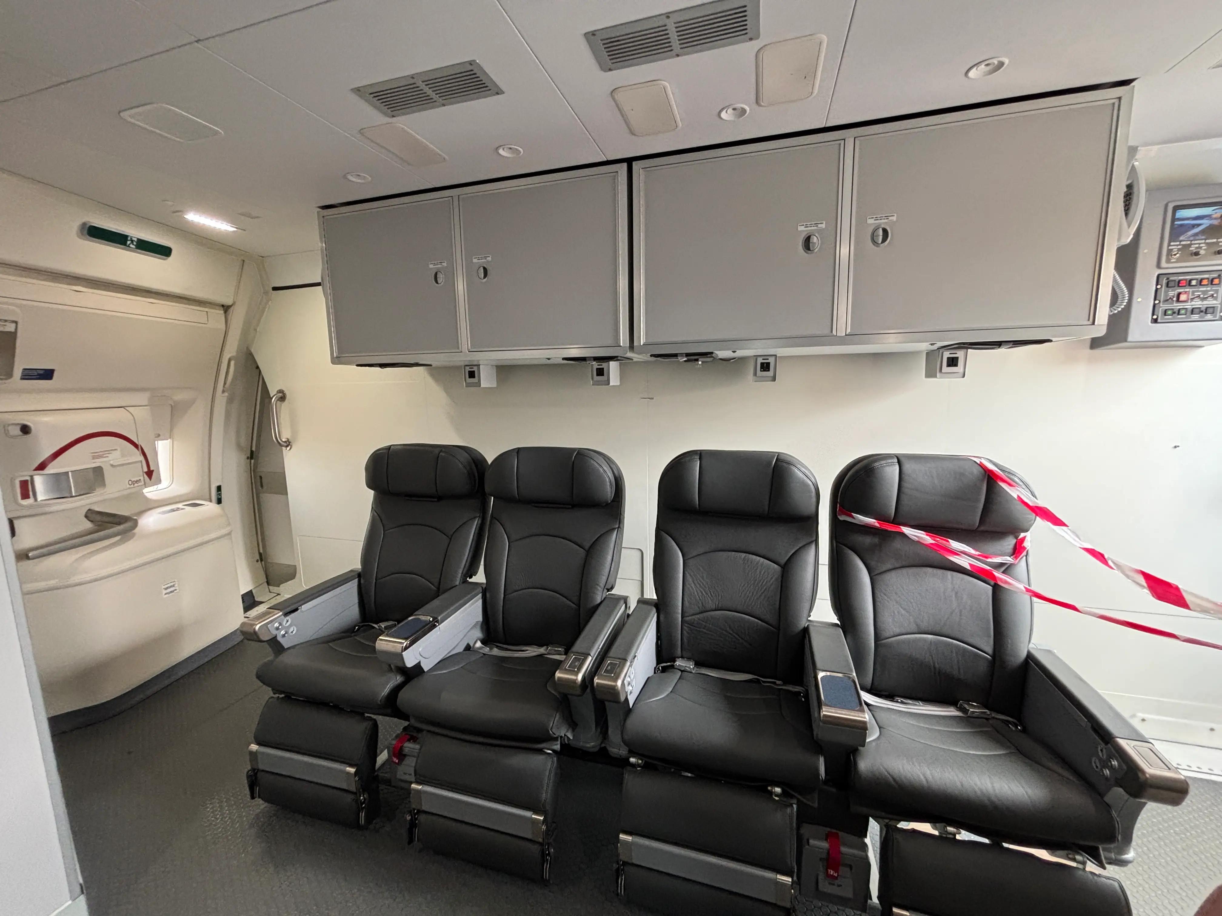 A wide view of four chairs and storage bins at the front of a DHL Boeing 777