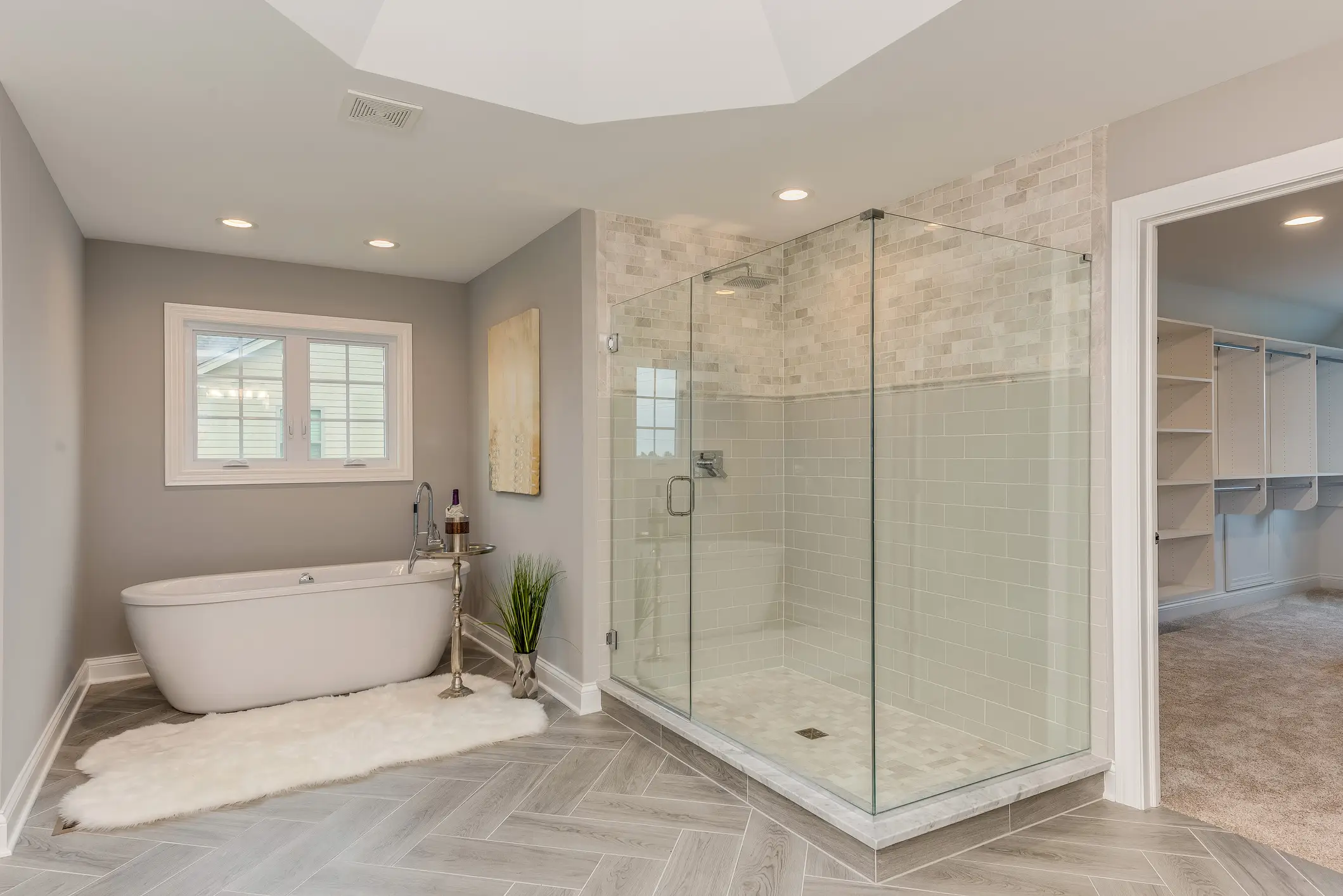 One rug in bathroom with small metal table next to it and large glass shower