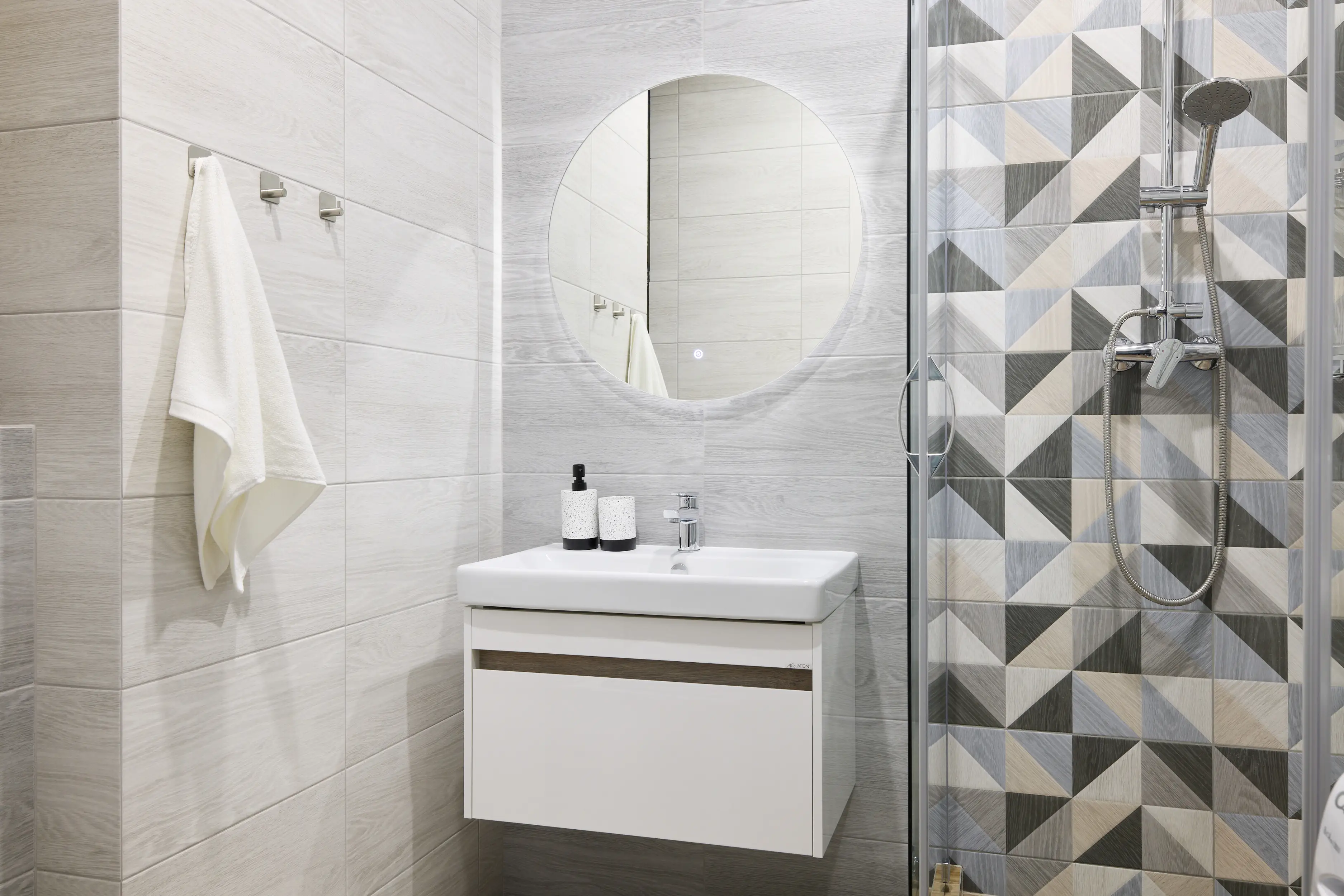 bathroom with geometric tile, small backlit round mirror, floating white sink