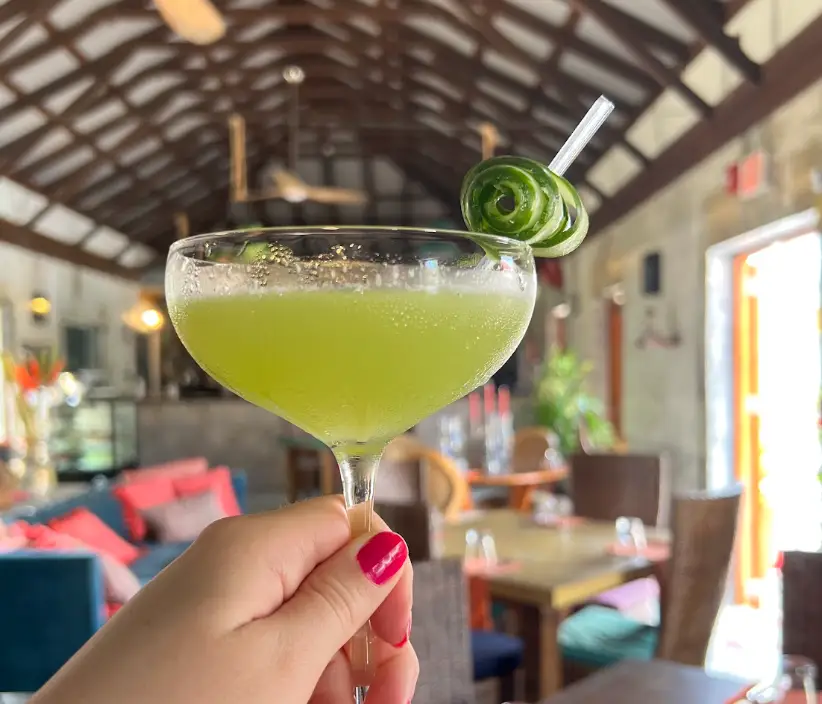 A hand holding up a green drink in a cocktail glass while on vacation.