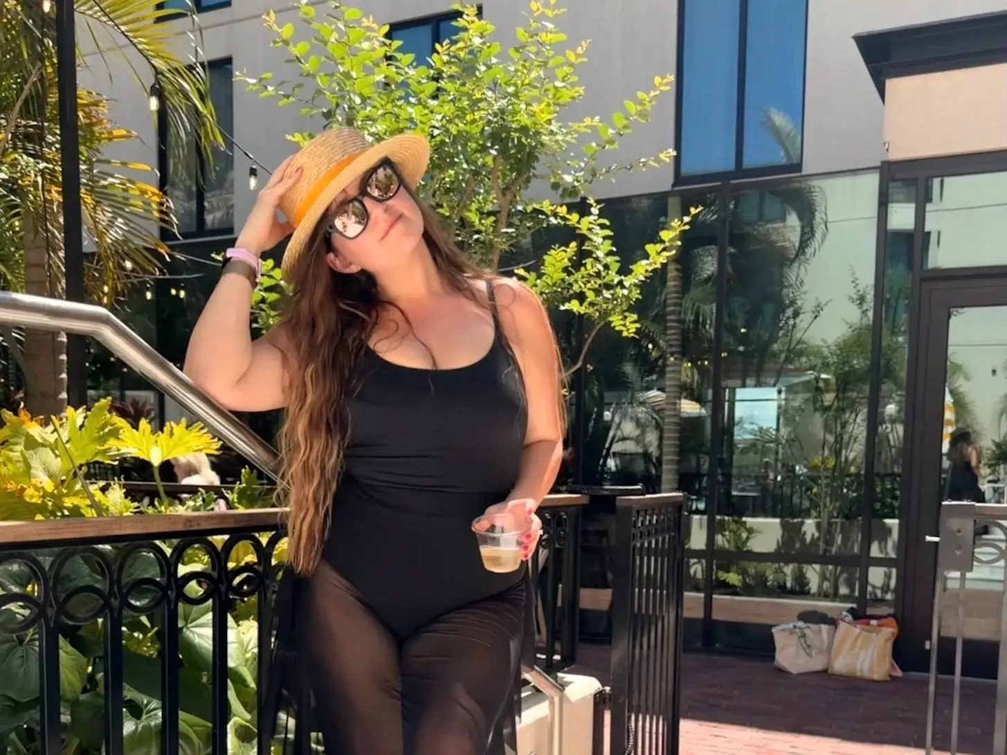 The writer wearing a black swimsuit and straw hat and standing in a beachy area.