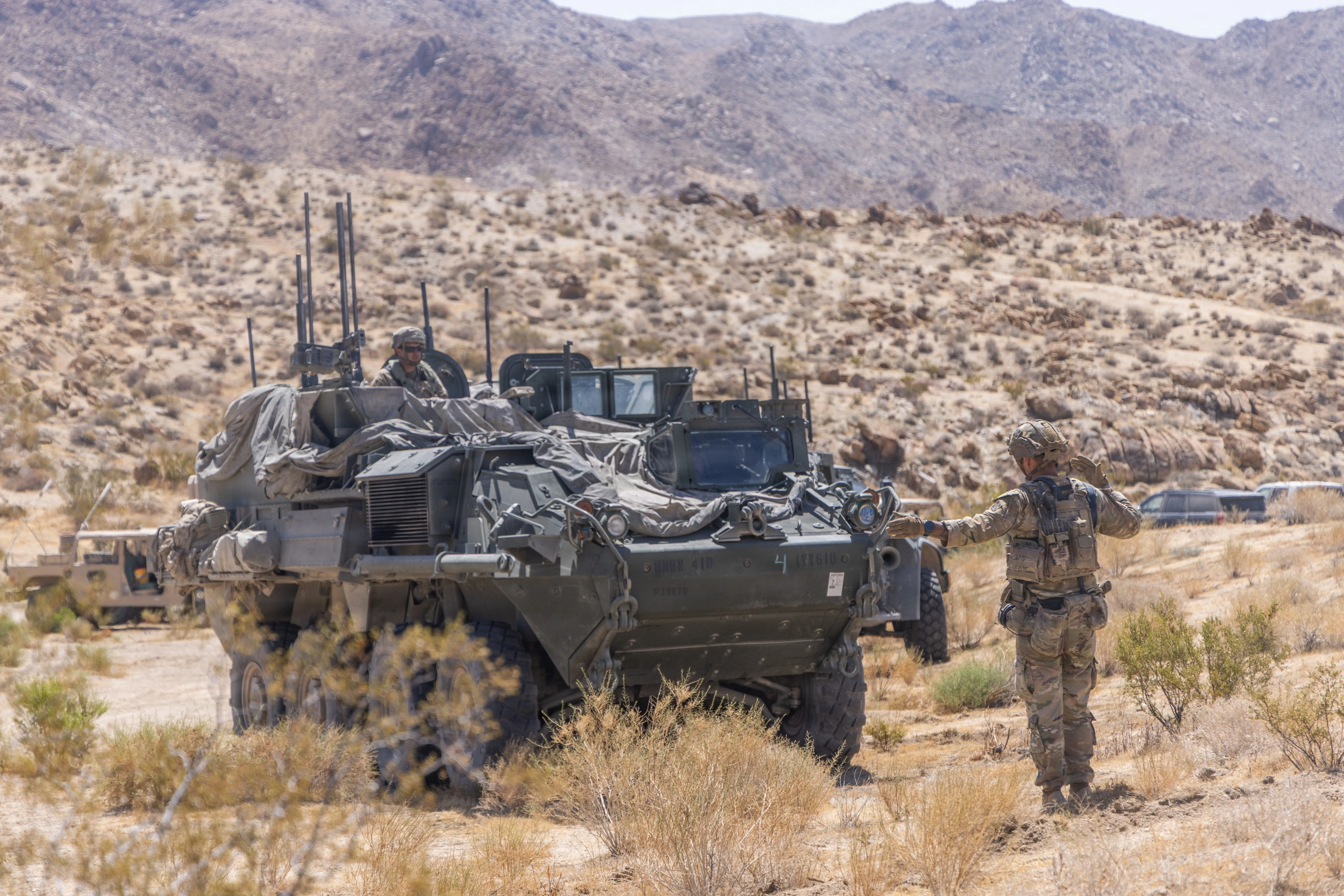 A US Army Stryker is parked in the desert. Soldiers stand on the side of it.