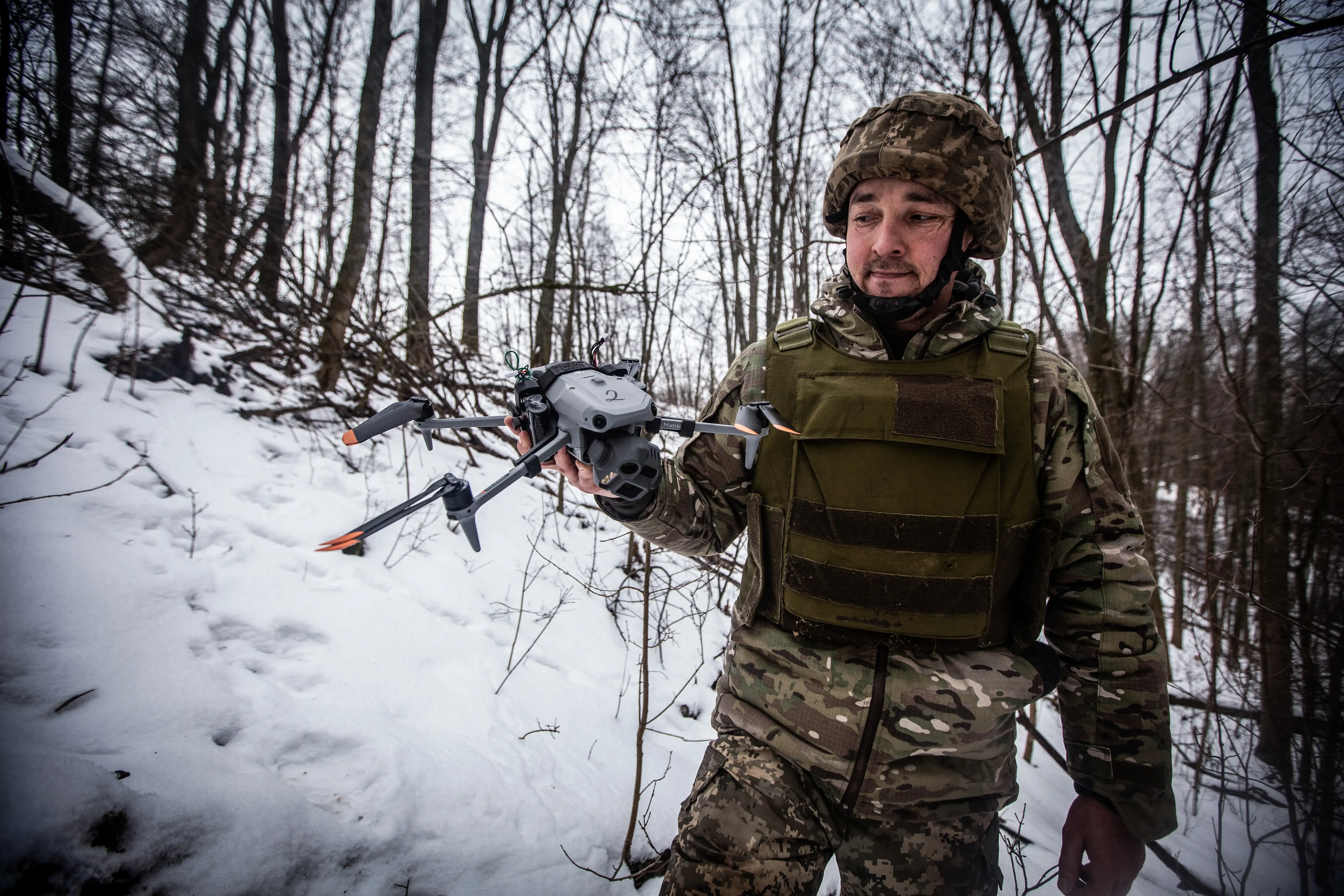 A Ukrainian soldier holds a quadcopter in a winter forest.