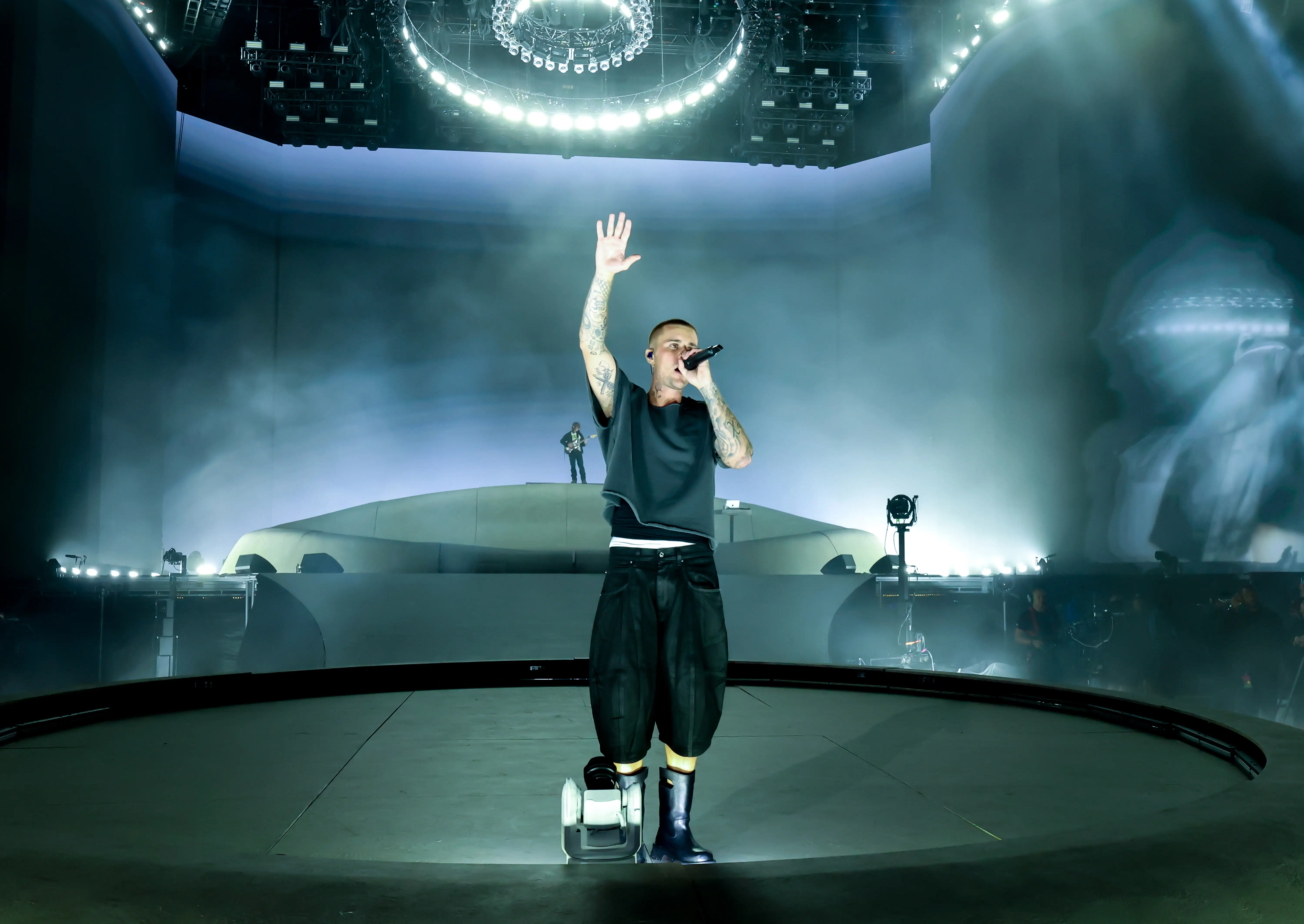 Justin Bieber sings into a handheld microphone on a large stage at Coachella under bright circular lighting.