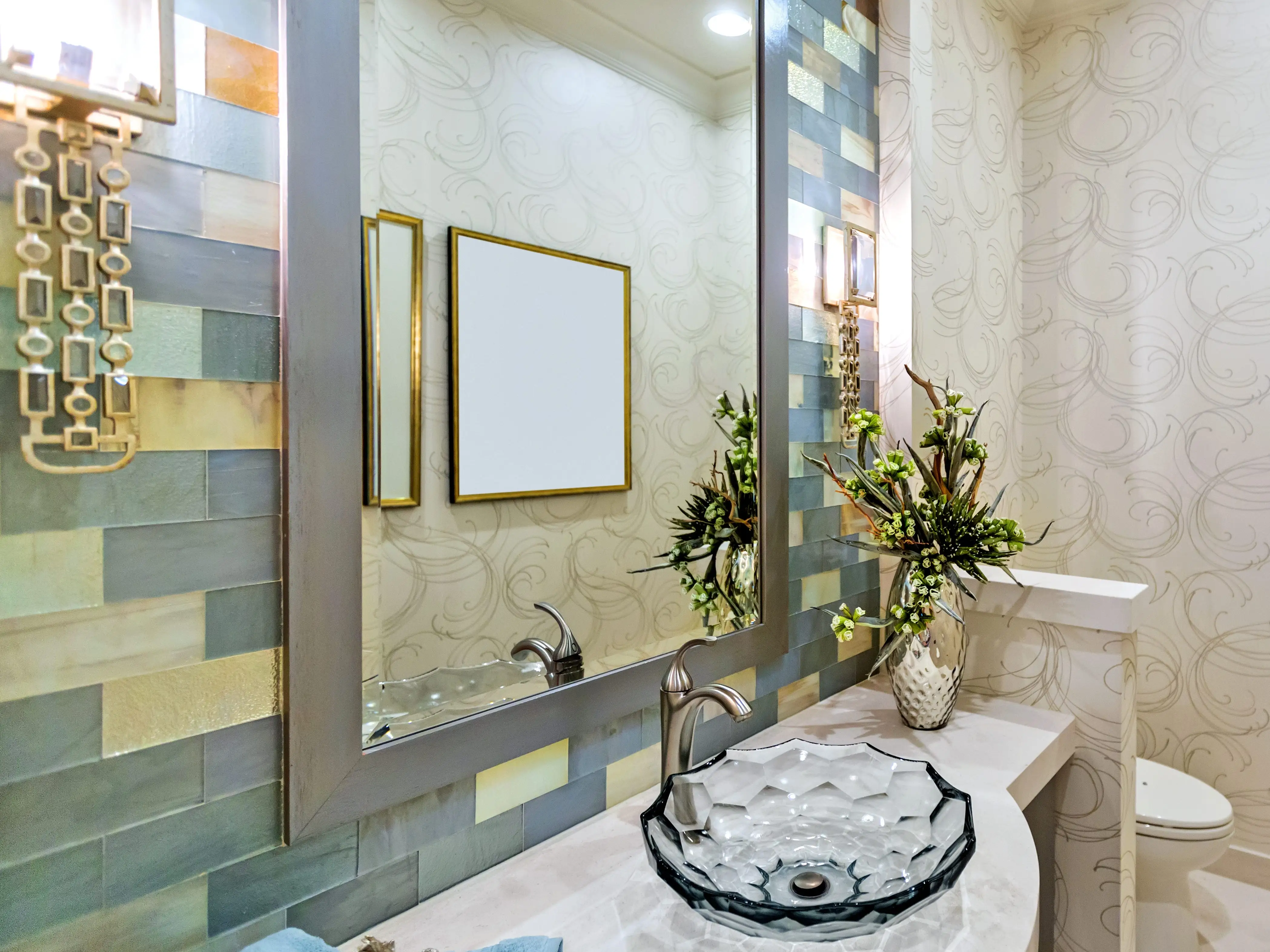 A powder room featuring a wall with yellow, green, and teal tiles and a white wallpaper with gray swirls.