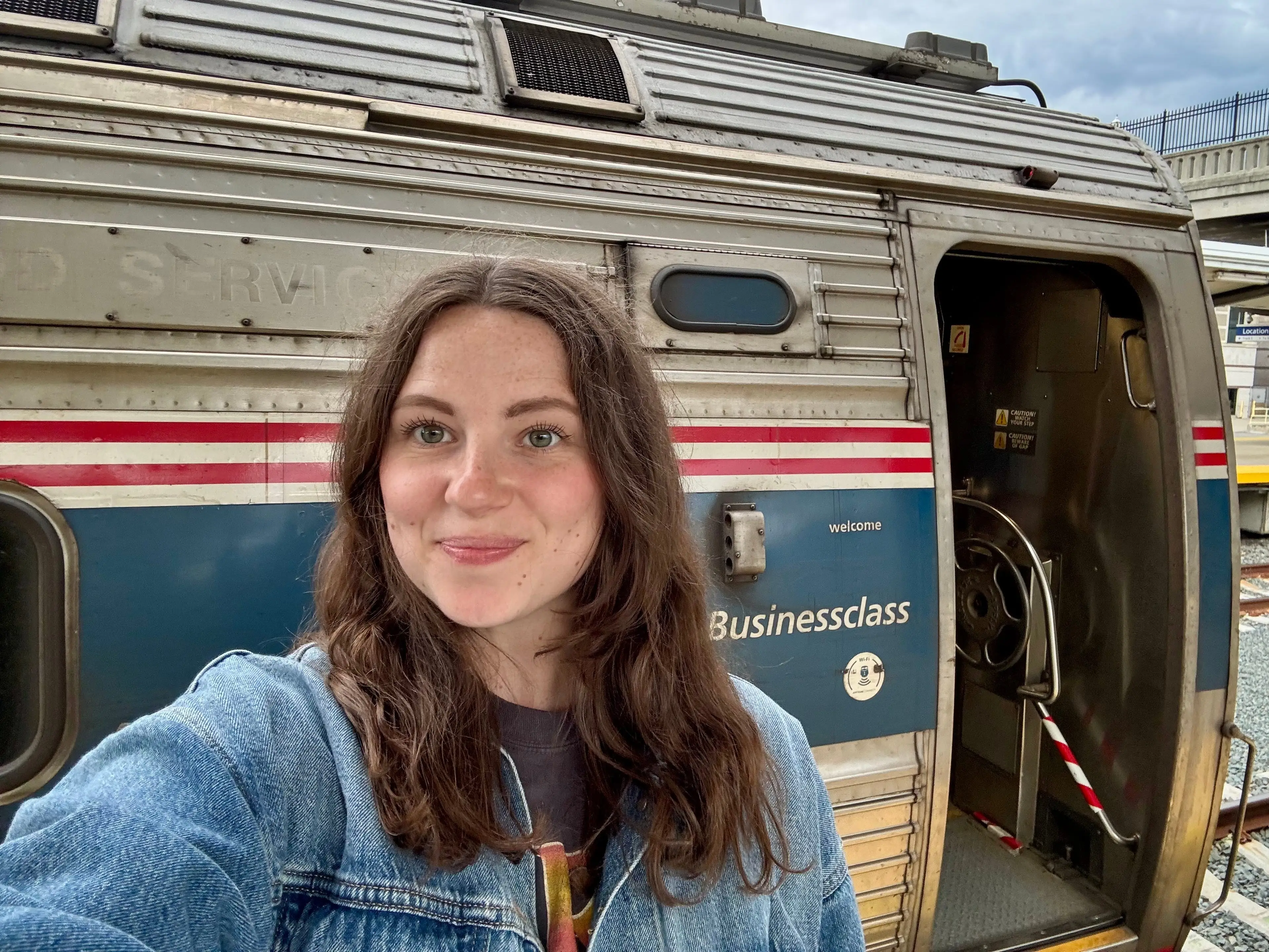 A woman takes a selfie beside an open Businessclass train car at a station platform.