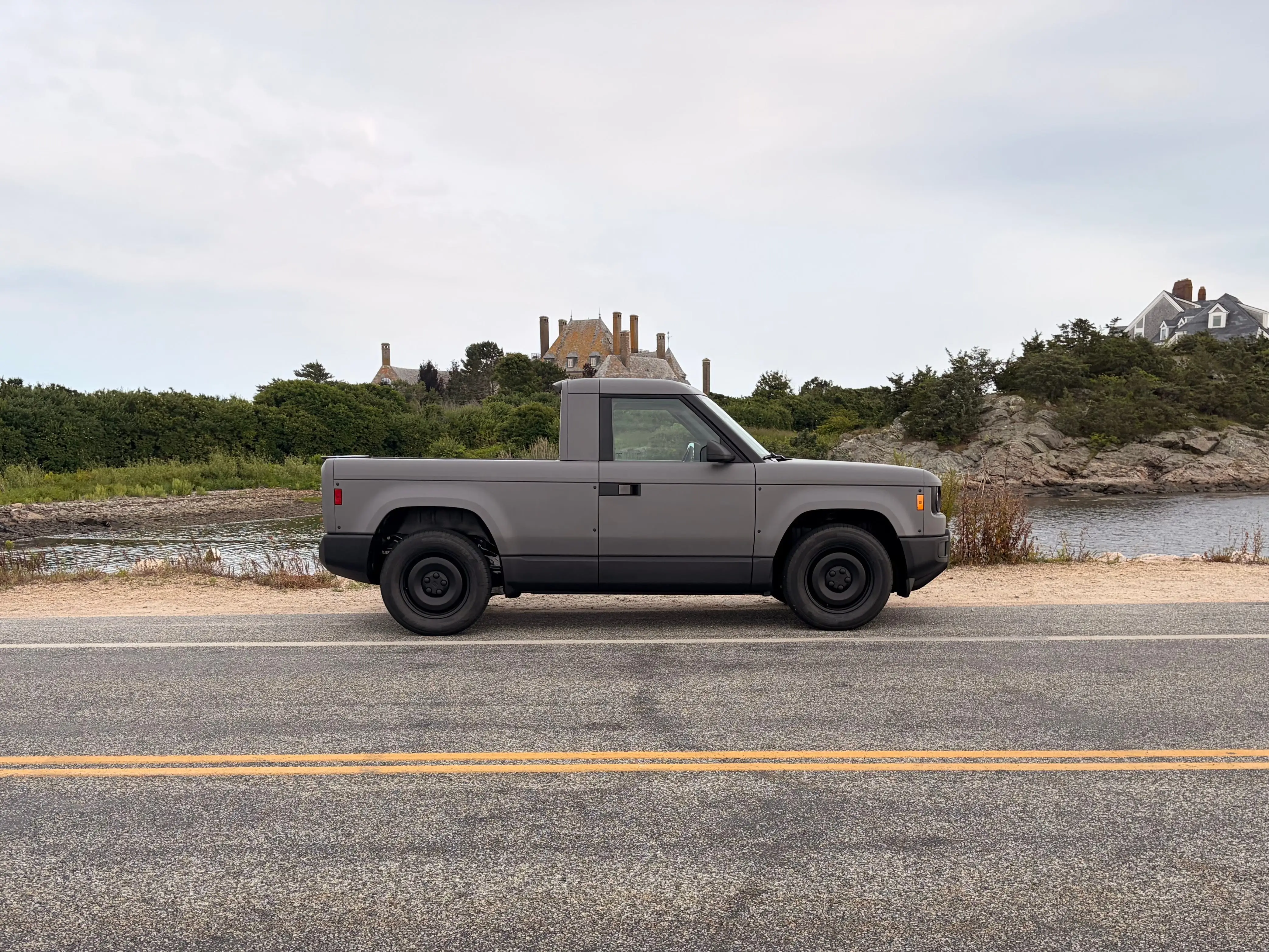 A gray Slate truck is parked on the side of a road. There are some beachfront mansions in the background.