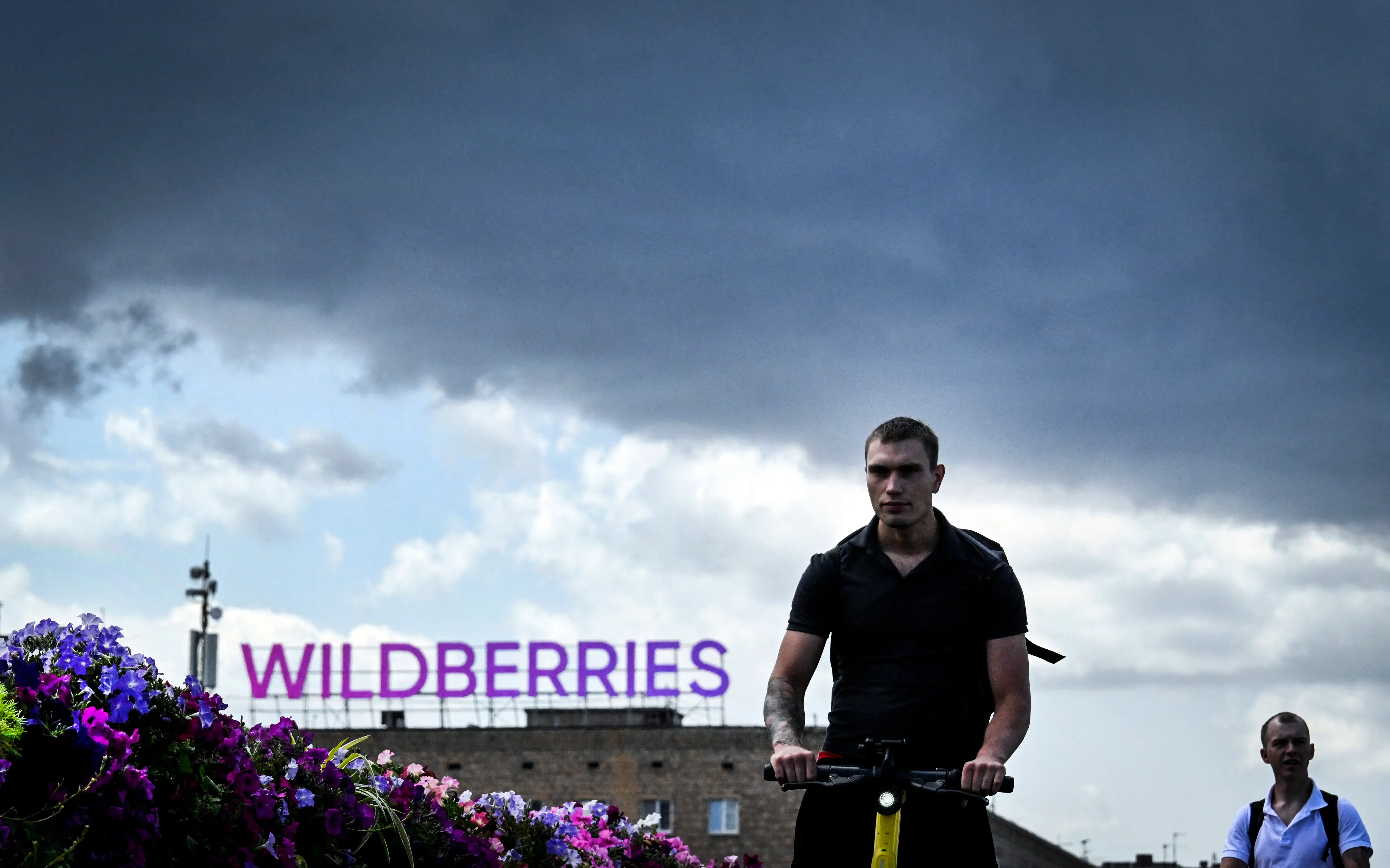 A man operates a scooter past a WildBerries building.