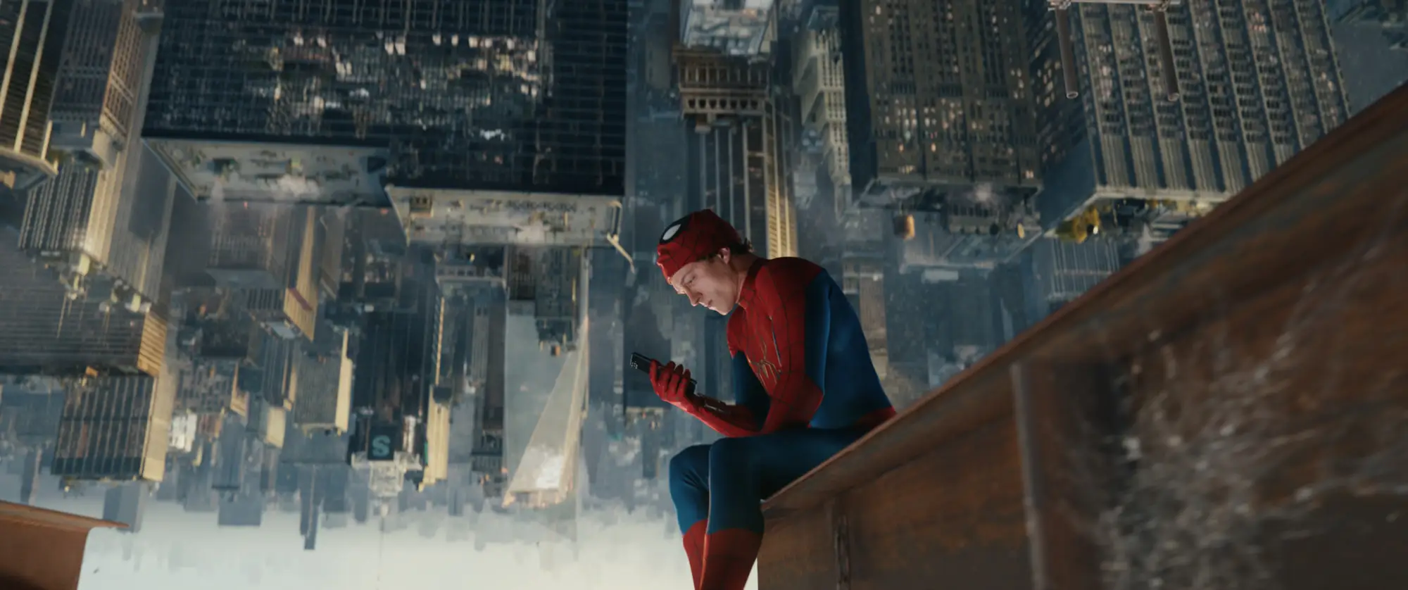 Tom Holland looking at his phone upside down on a steel beam in Spider-Man suit