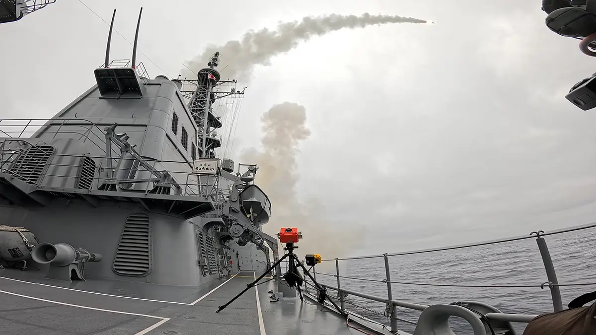 A Tomahawk missile flies over a Japanese destroyer in the ocean.