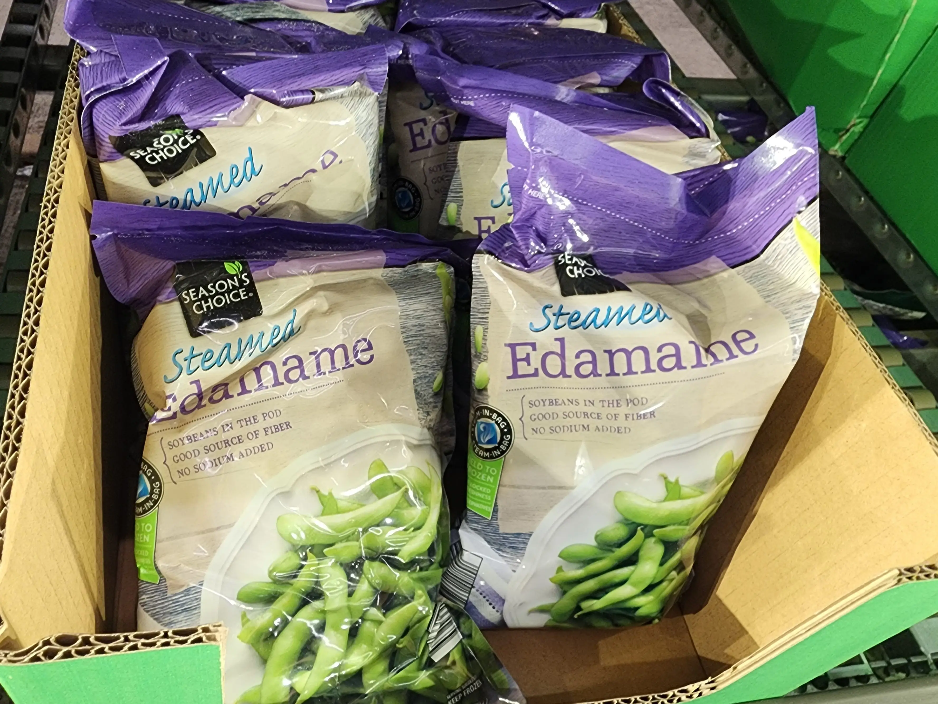 Several bags of Season's Choice steamed edamame sitting in a cardboard box at Aldi.