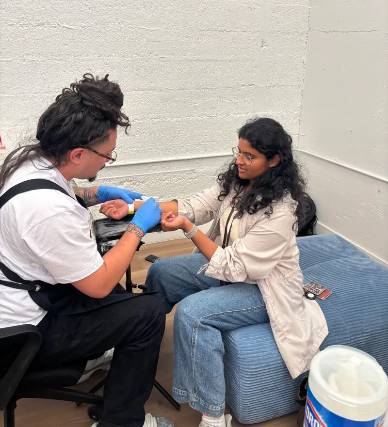 A man in blue gloves applying a tattoo to a woman's wrist.