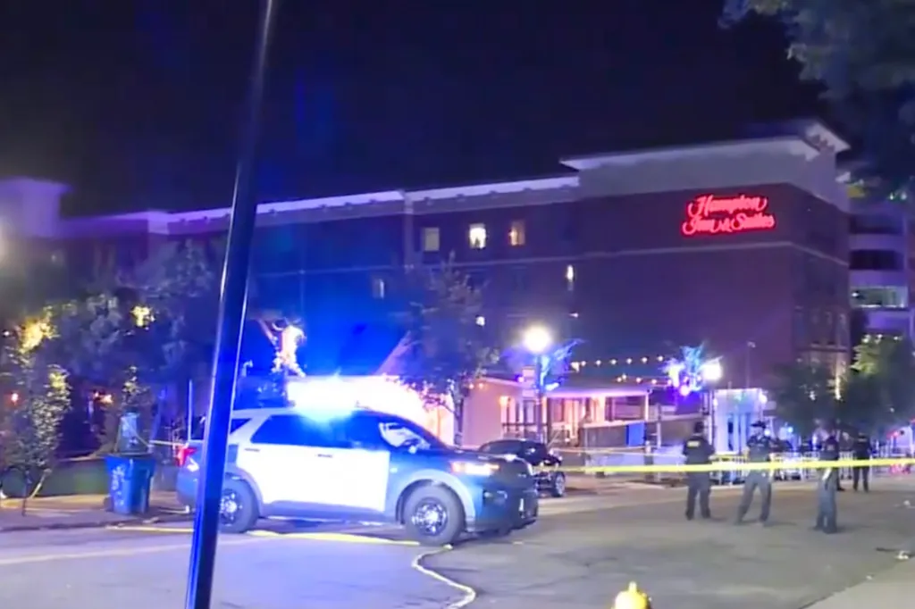 Police block off a street at night in front of a Hampton Inn & Suites with yellow tape and a police vehicle.