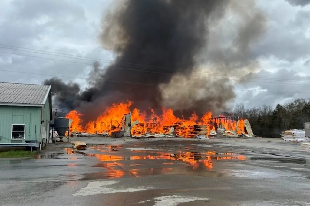 Lumber mill engulfed in flames, with thick black smoke billowing into the sky.